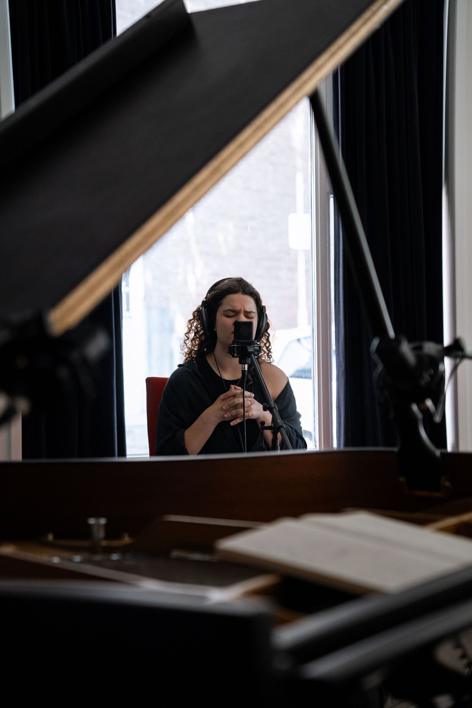 Female vocalist with headphones sings into a microphone in a recording studio.