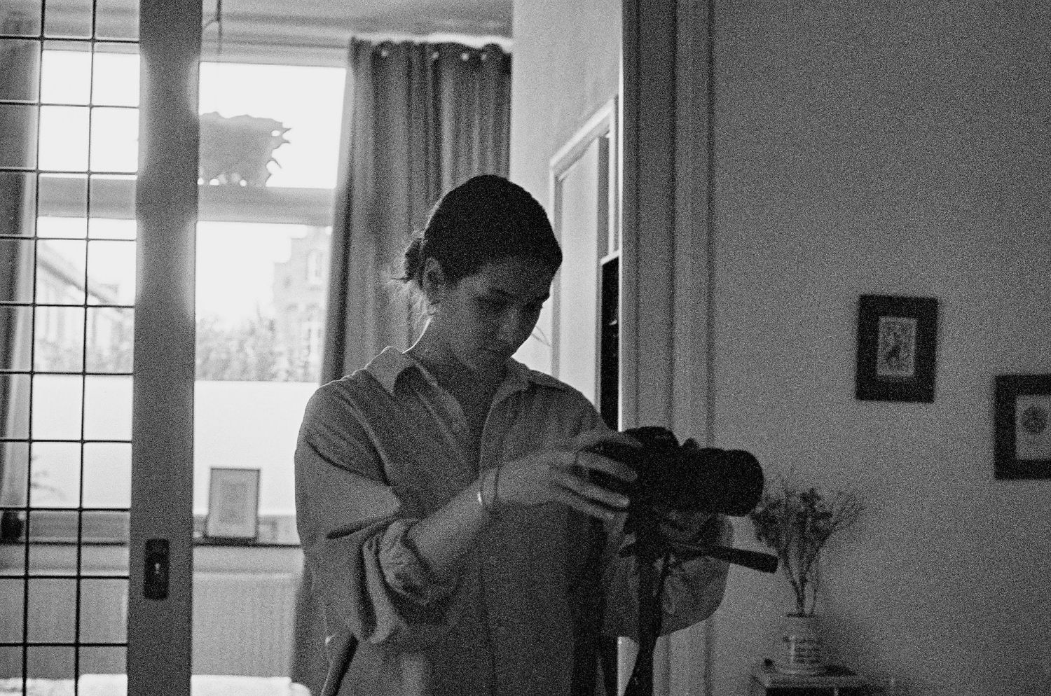 Black and white self-portrait of photographer taking mirror selfie with camera indoors.