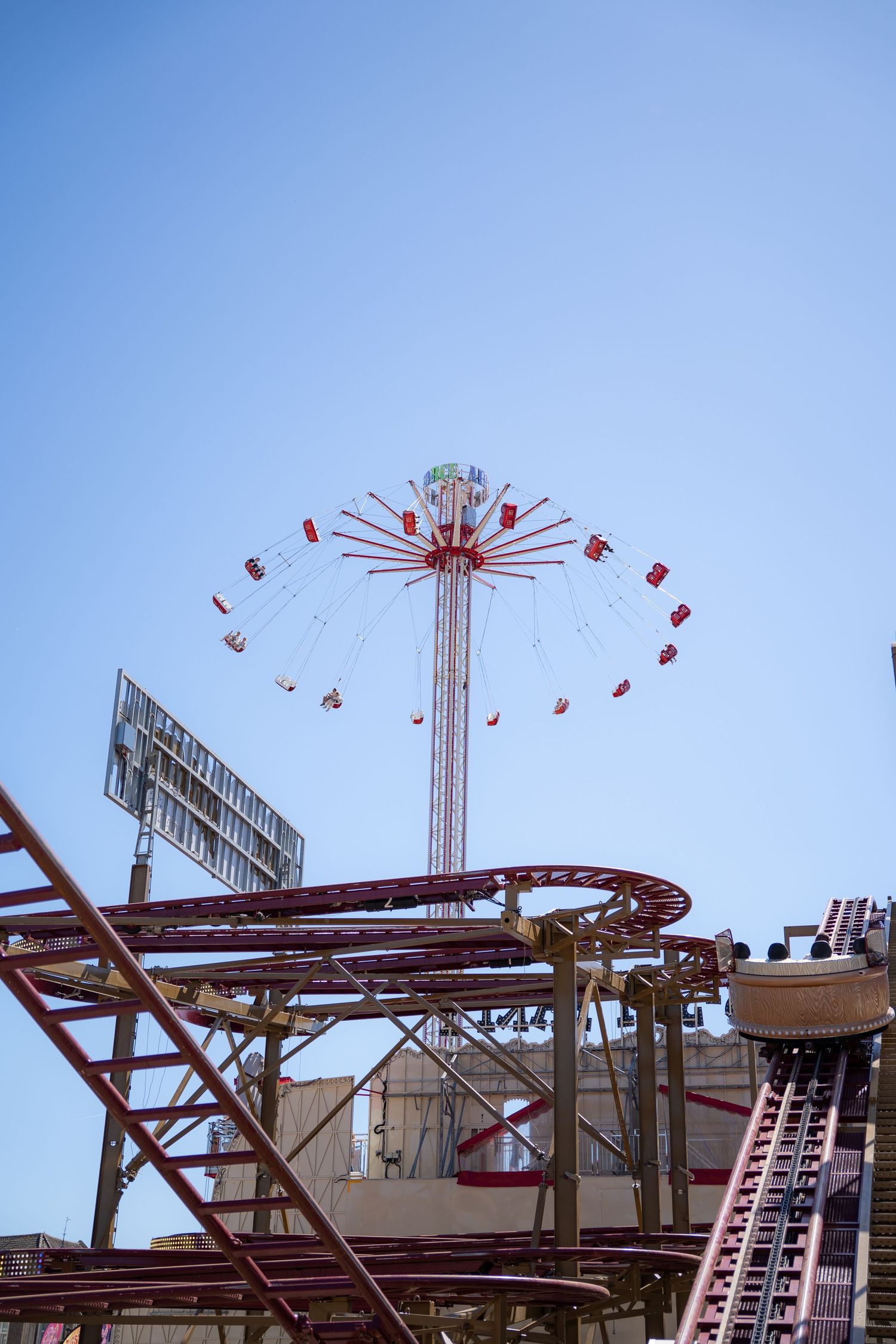 A tall chain swing carnival ride and roller coaster tracks set against a bright blue sky at an amusement park.