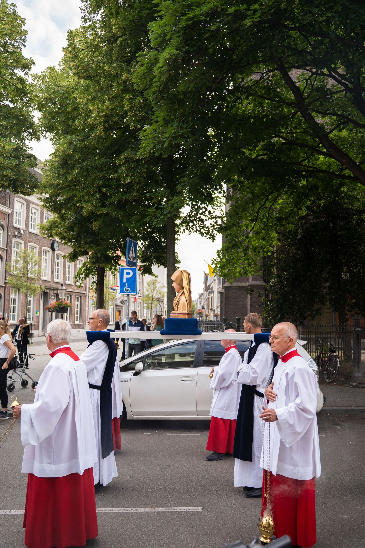 Clergy in white and red robes gather around a golden statue during an outdoor religious procession.