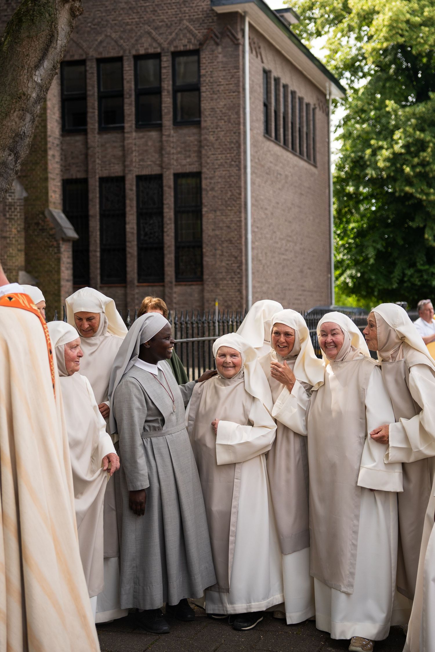 Group of nuns in white habits laugh together outdoors during religious gathering.