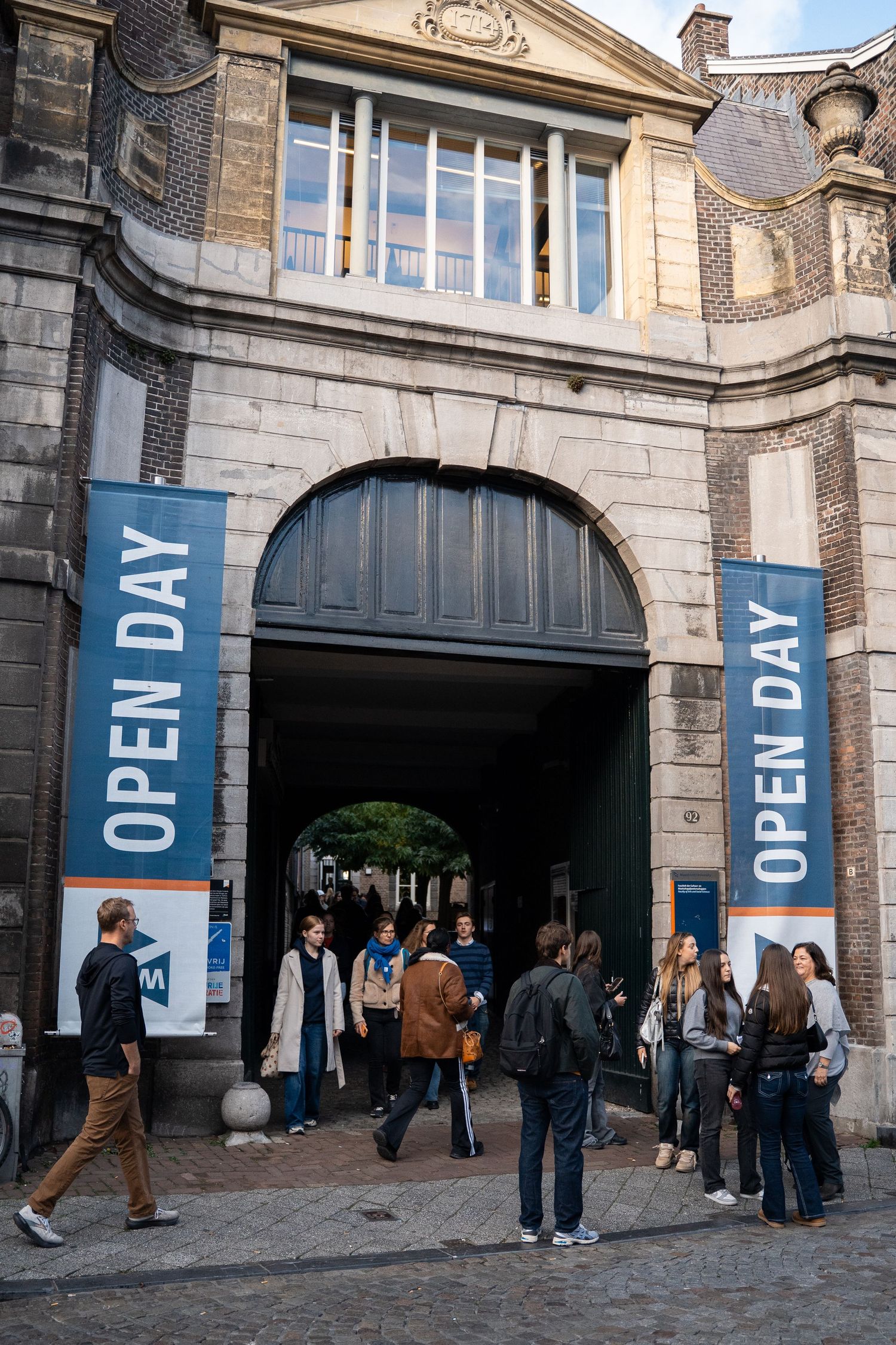 Students gather at an arched entrance with Open Day banners at Maastricht University.