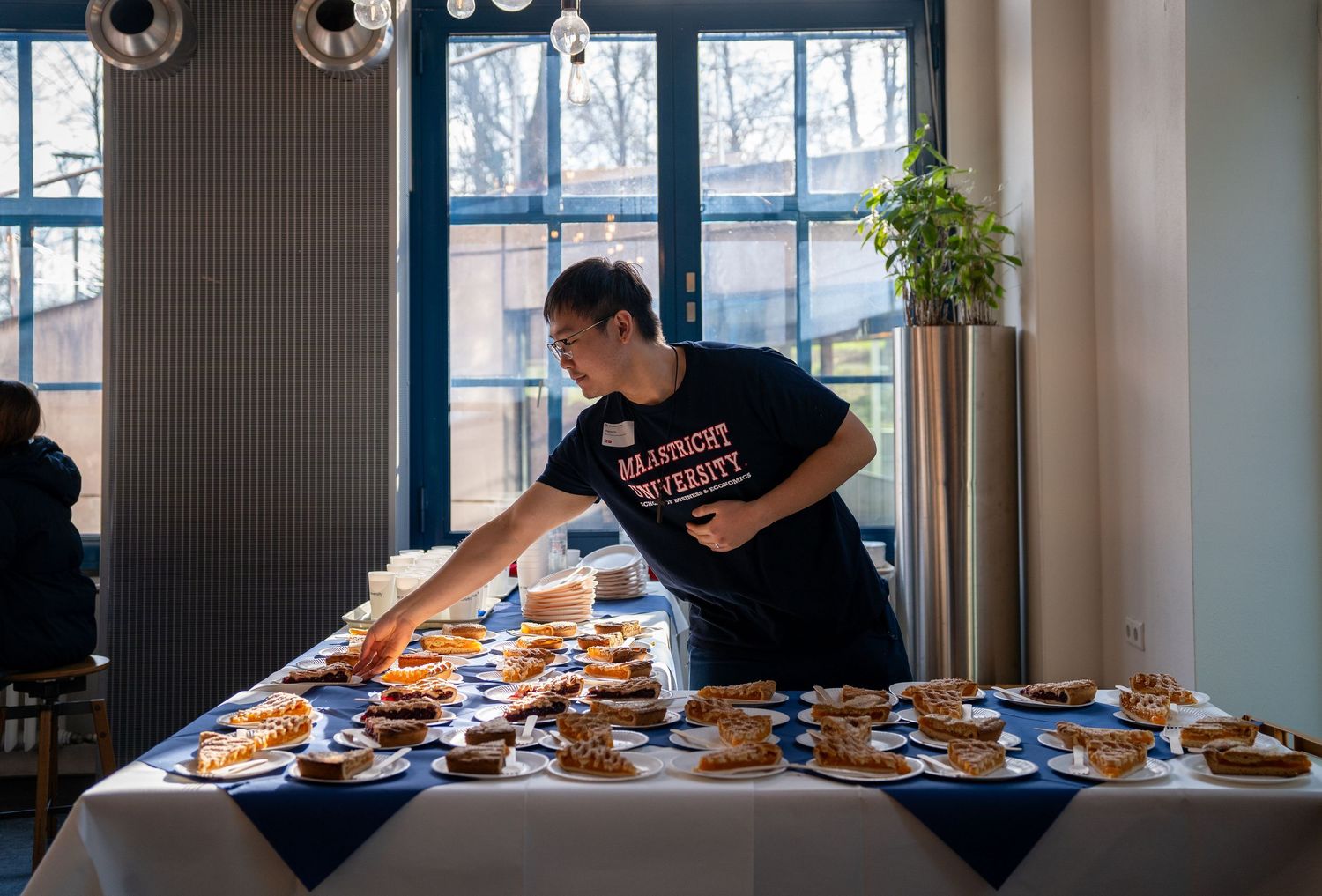 Maastricht University staff member arranges pastries on a table at a university open day catering event.