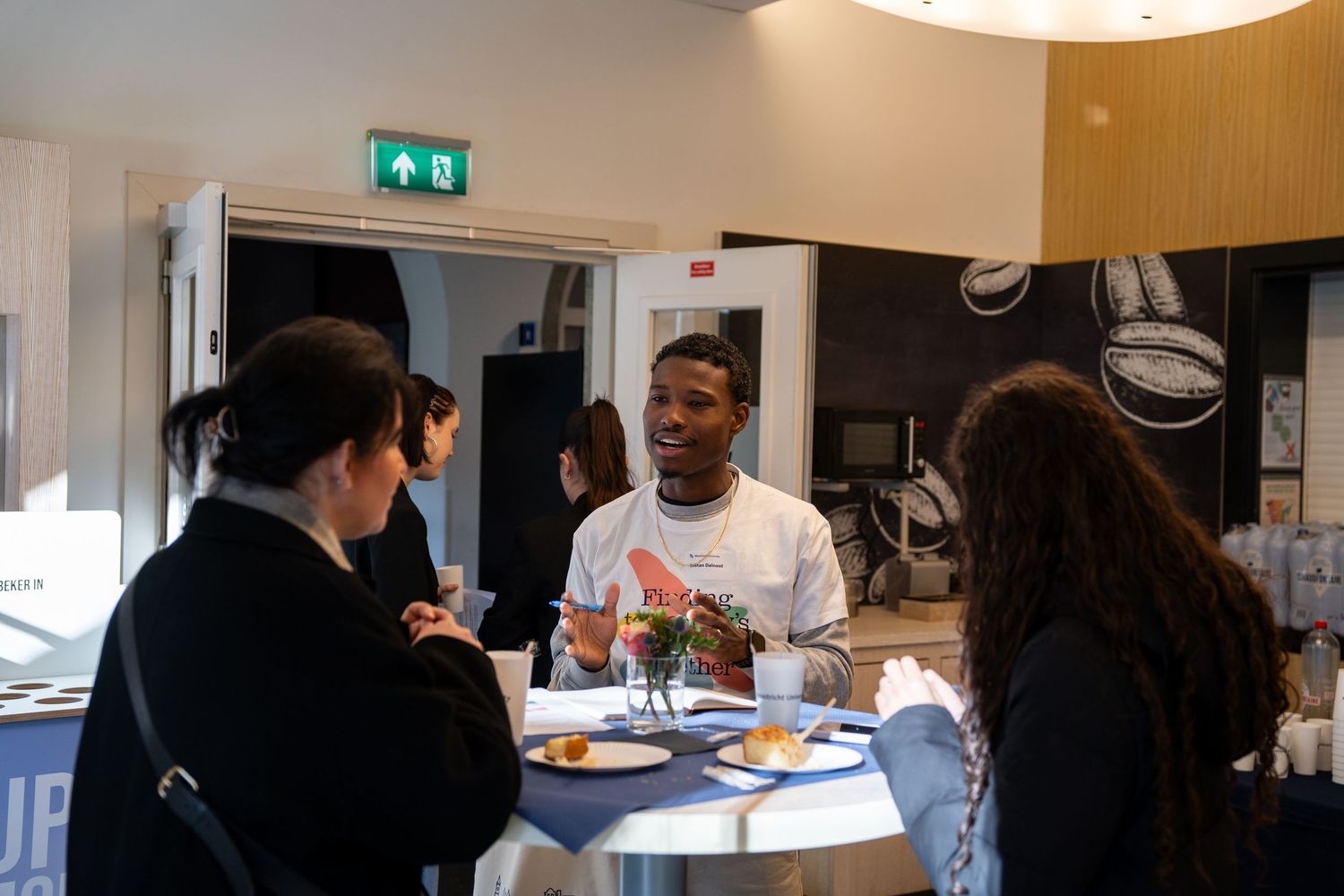 Students chat and enjoy refreshments at a Maastricht University open day networking event indoors.