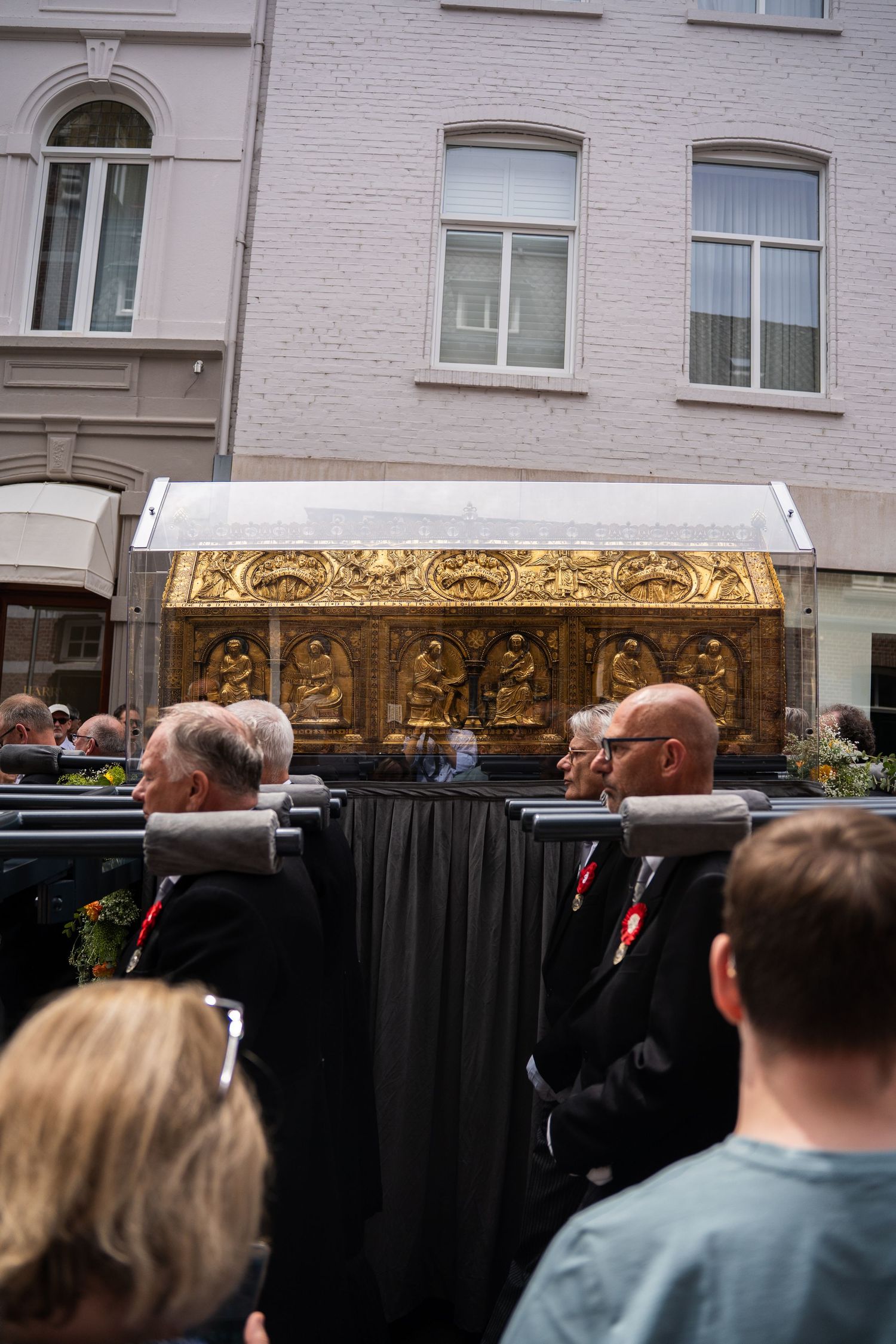 Close-up of ornate golden reliquary shrine carried by men in black during a religious procession.