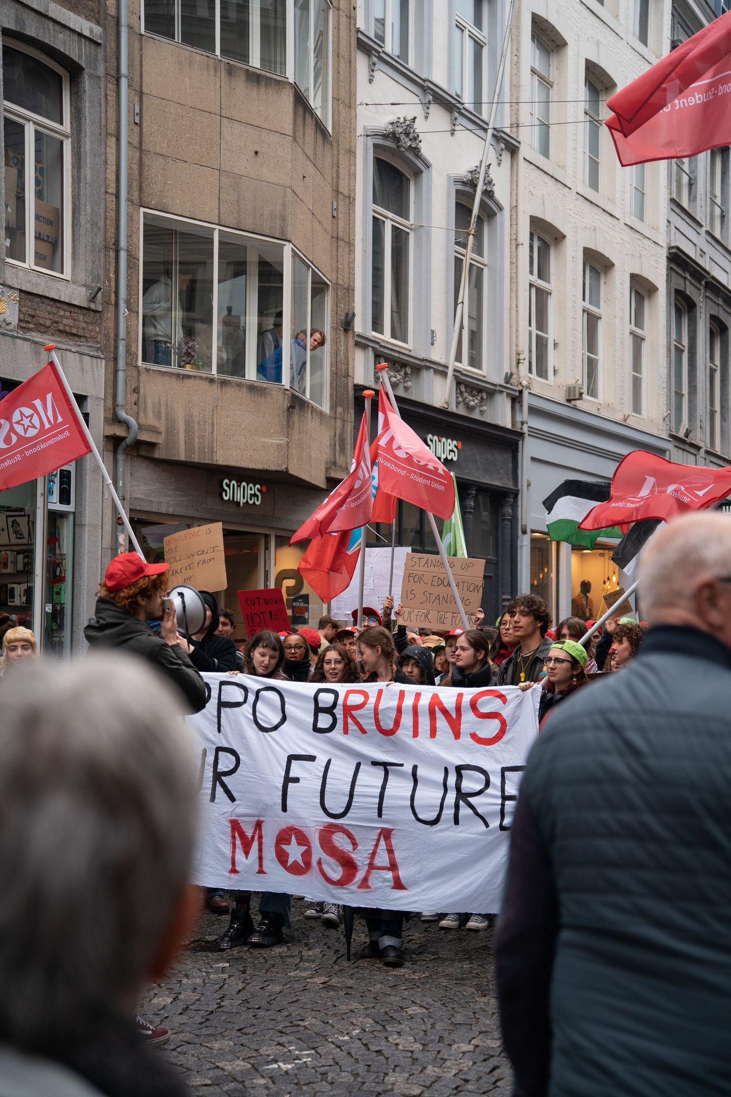 Protesters marching with banner reading Future Mosa and red flags through a cobblestone street in Maastricht.