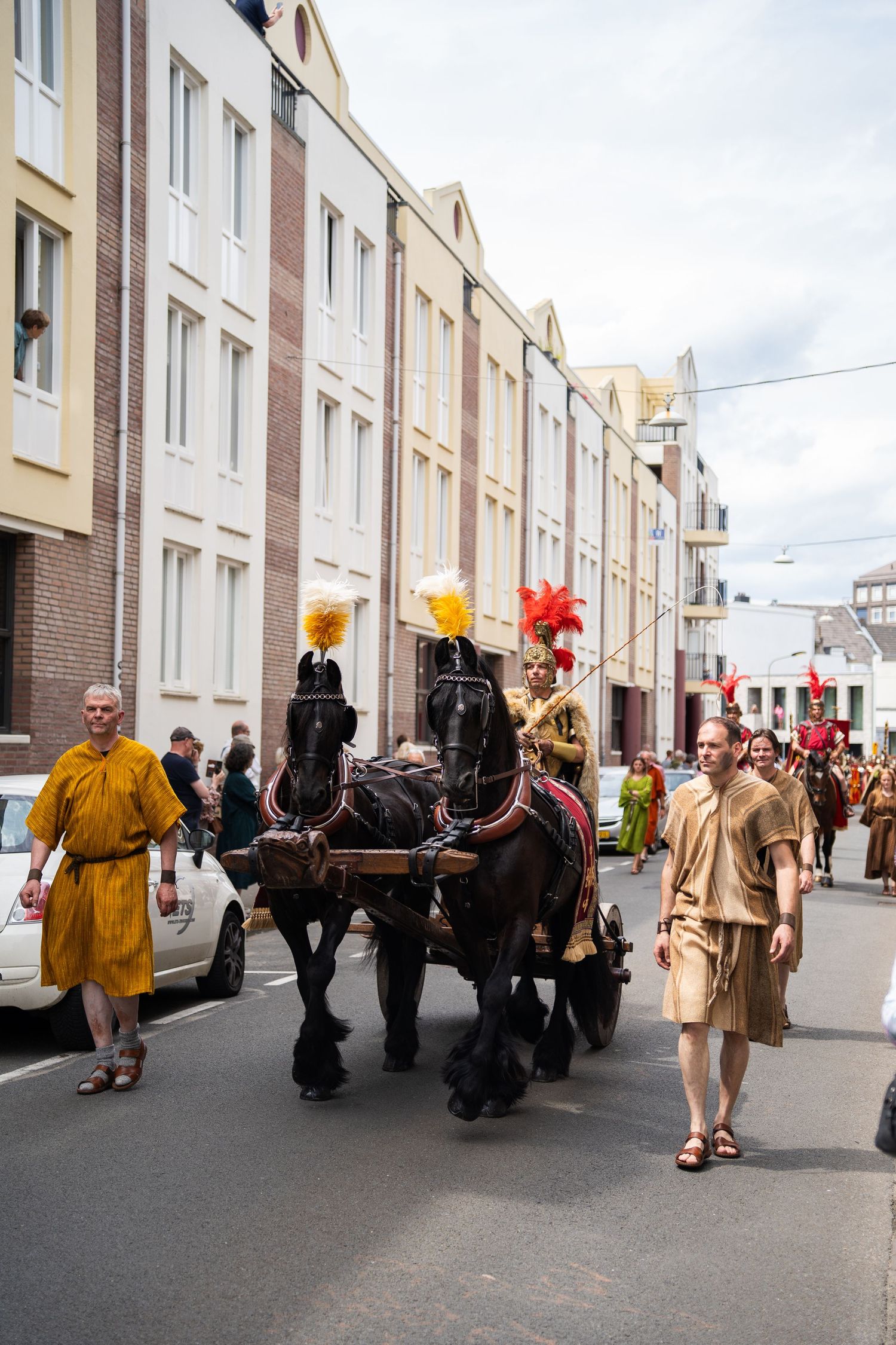 Horse-drawn carriage with Roman costumes leads a historical parade through city streets.