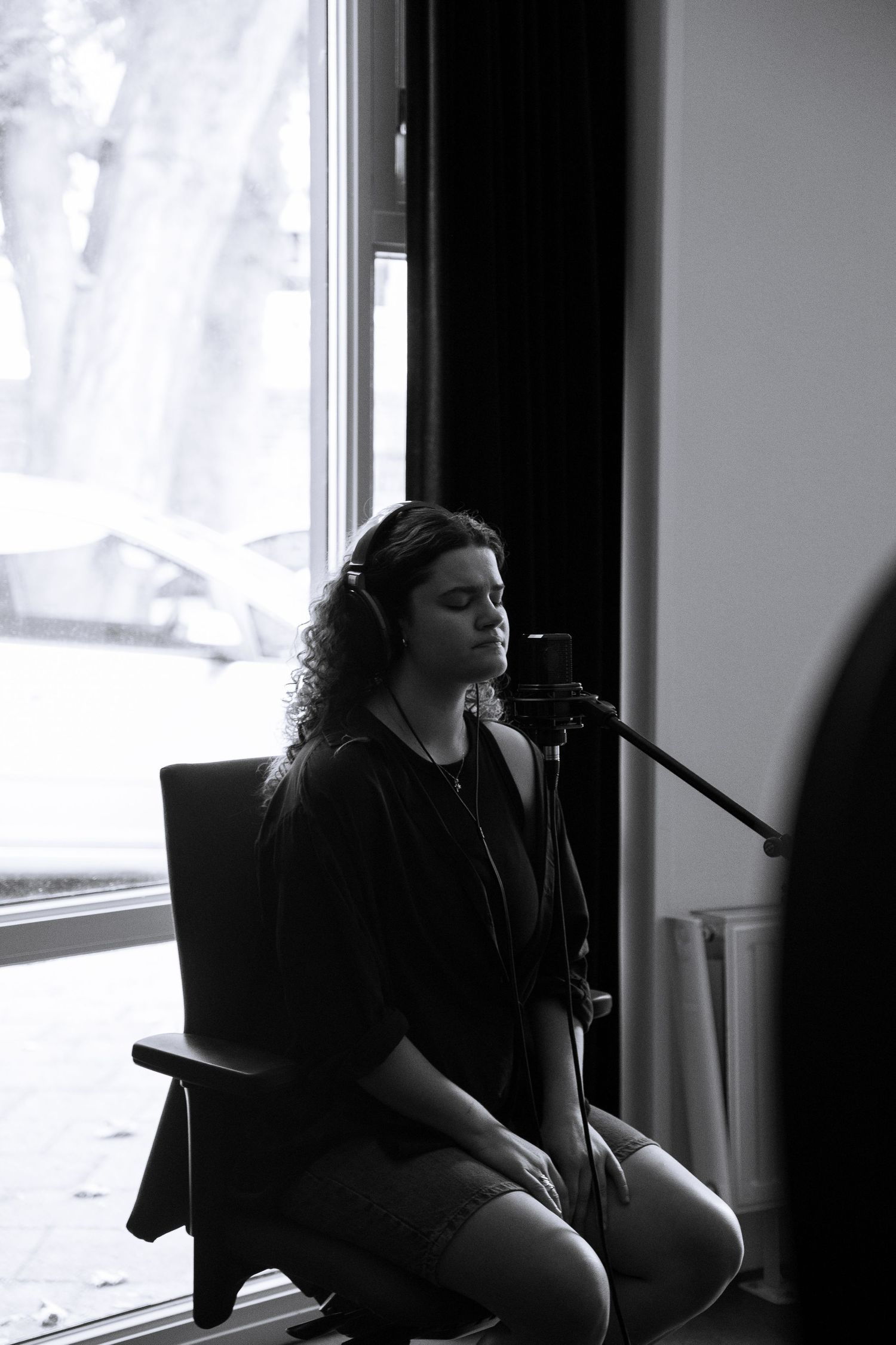 Black and white photo of a curly-haired woman singing into a studio microphone.