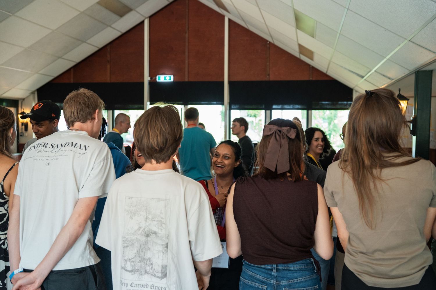 Young people socializing inside a venue hall with wooden ceiling during an indoor gathering event.
