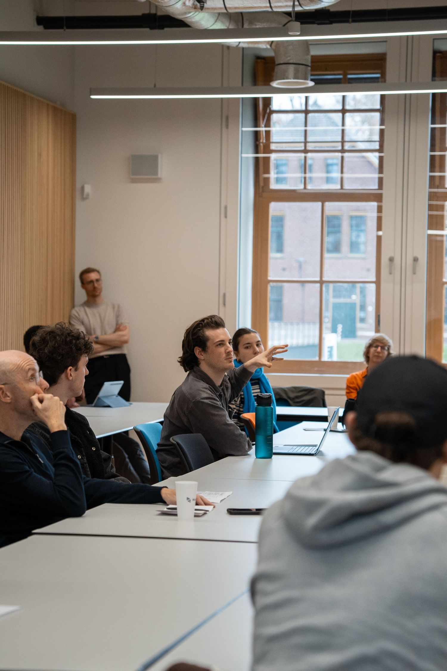 University students engage in discussion during a seminar in a bright, modern classroom with large windows.
