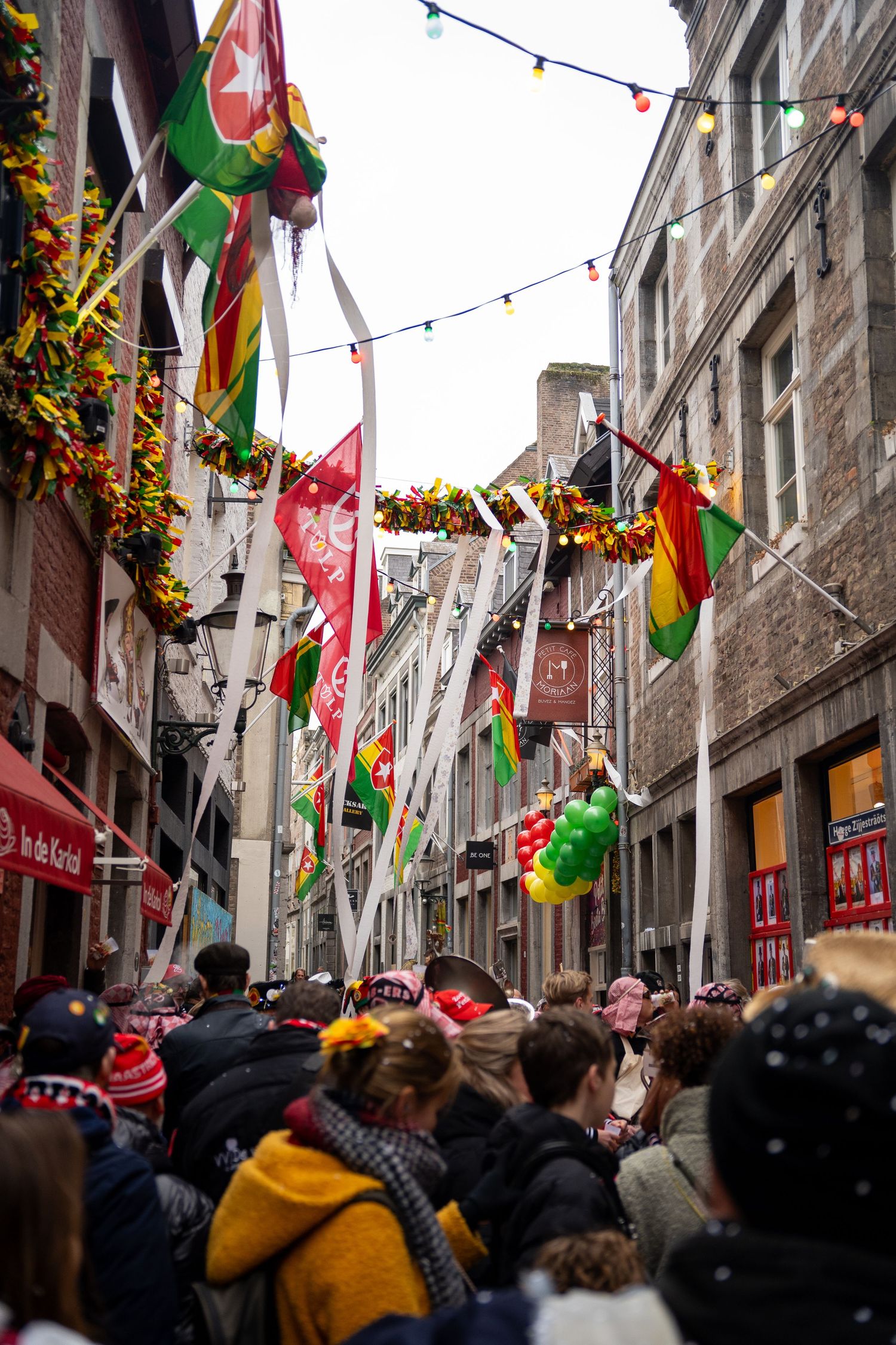 Crowded narrow street decorated with colorful flags and bunting during a carnival festival.