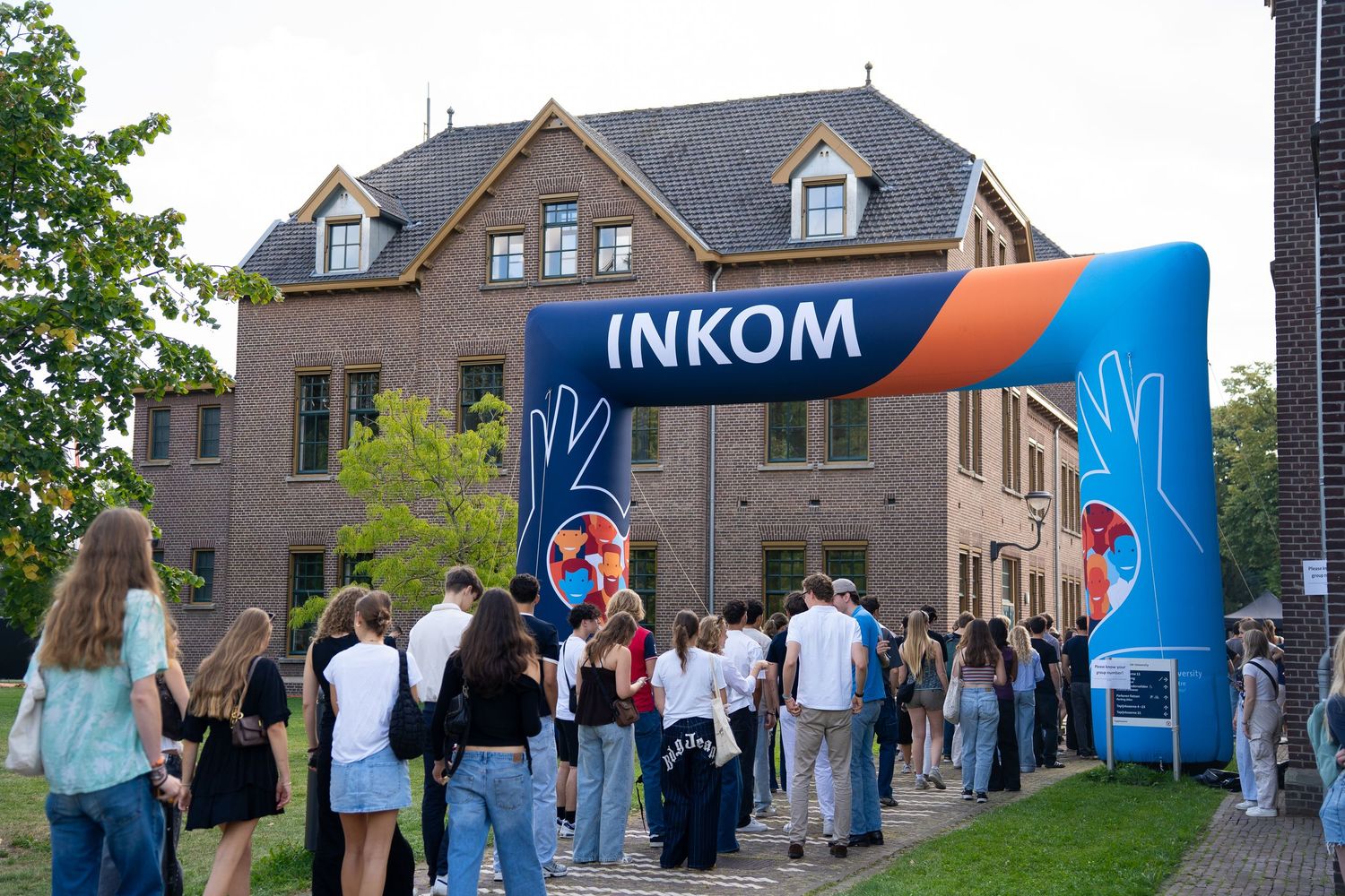 Students entering university orientation event through large inflatable INKOM archway entrance.