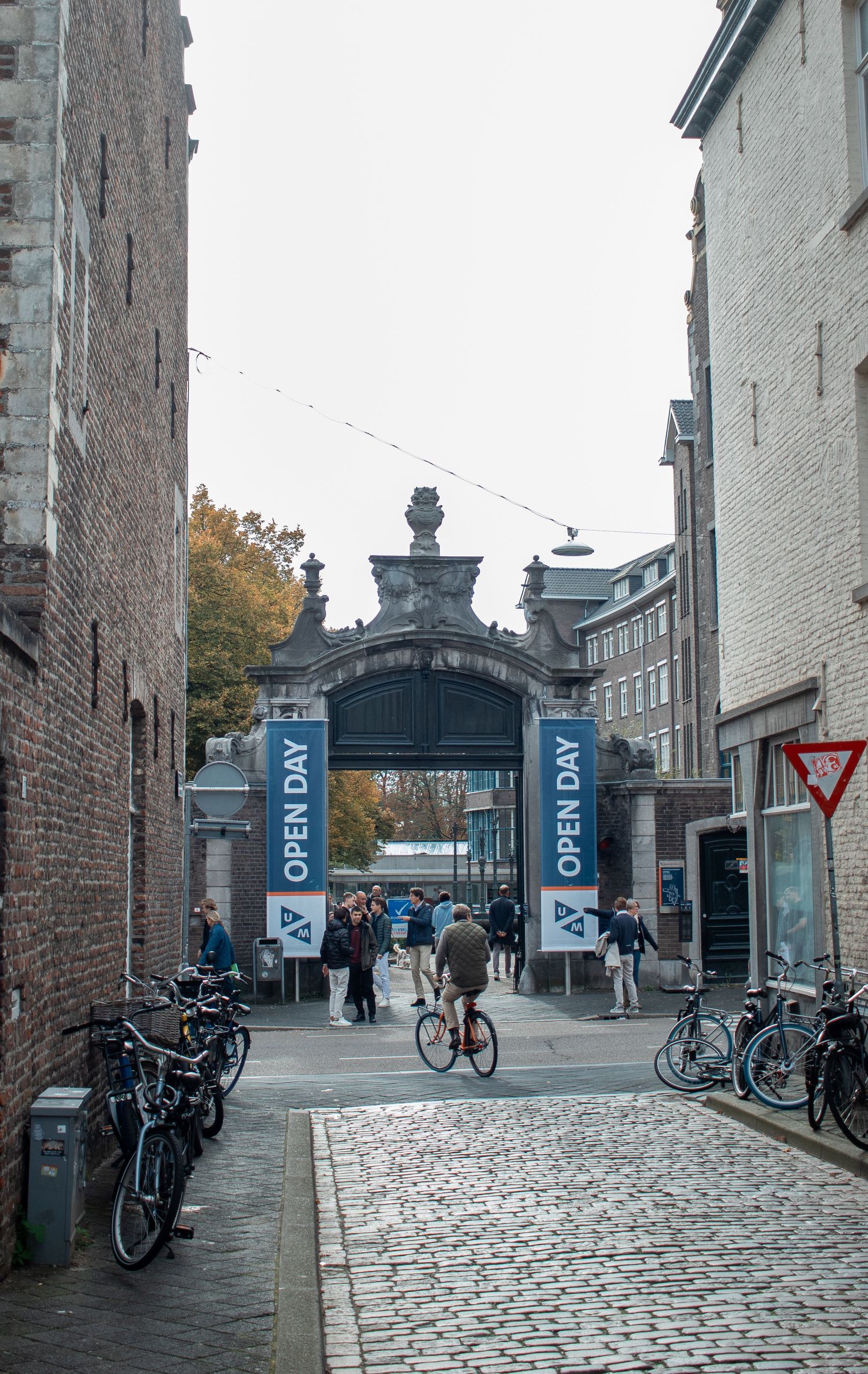 Cobblestone path leads to historic gate with Open Day banners at Maastricht University campus.