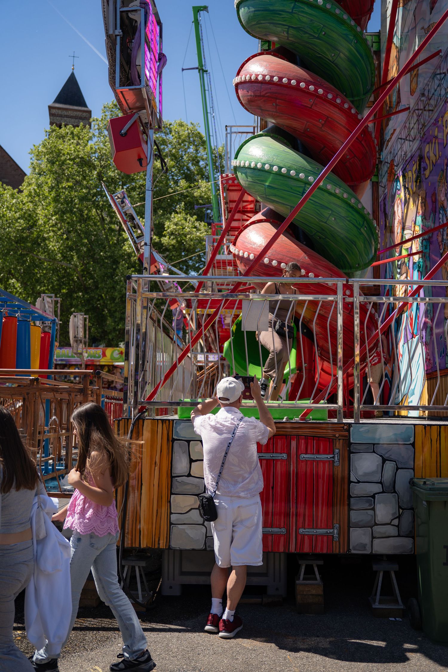 Visitors explore a vibrant fairground attraction featuring large colorful decorative elements on a sunny day.