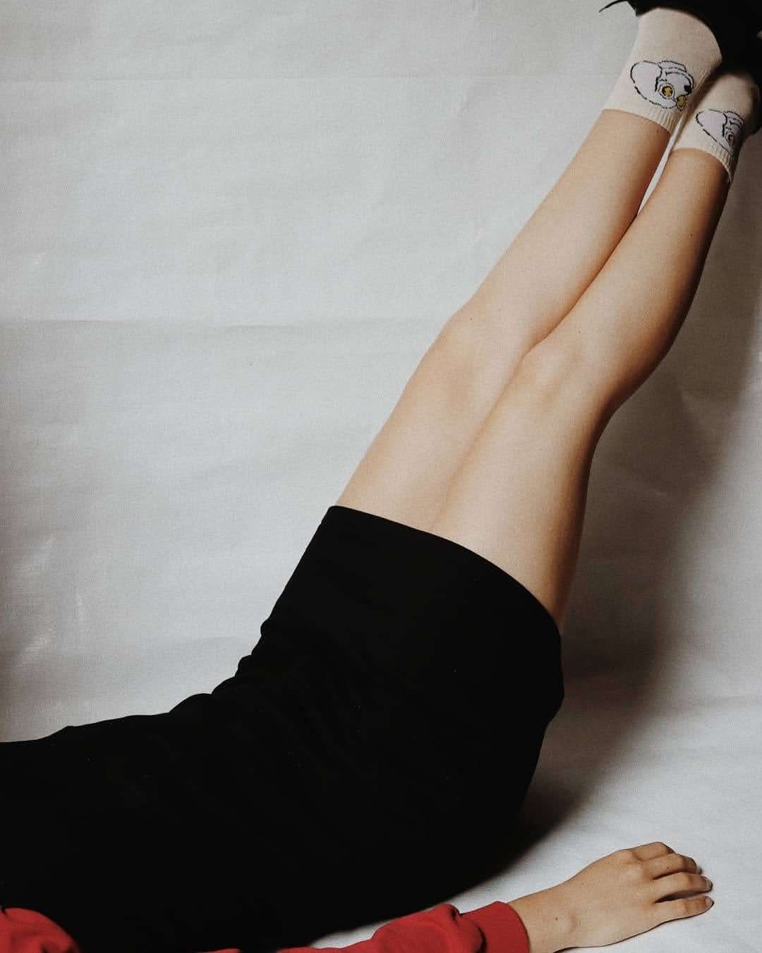 Person lying down with legs raised wearing black skirt and white sneakers on white background.