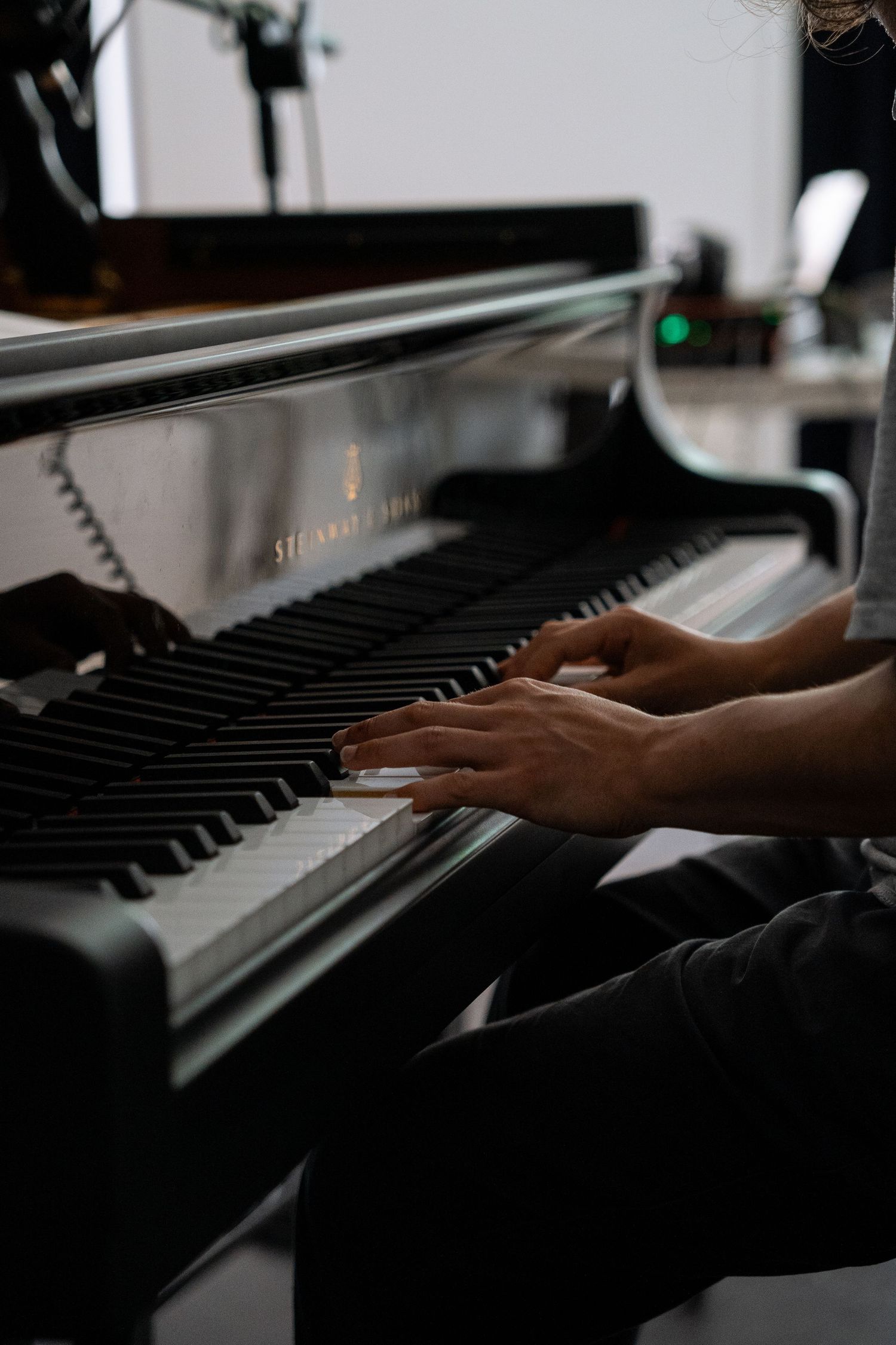 Close-up of hands playing a Steinway grand piano in a recording studio.