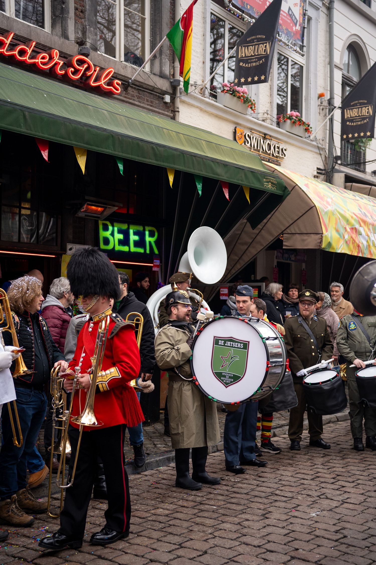 Brass band in uniform performing on a cobblestone street outside a beer pub.