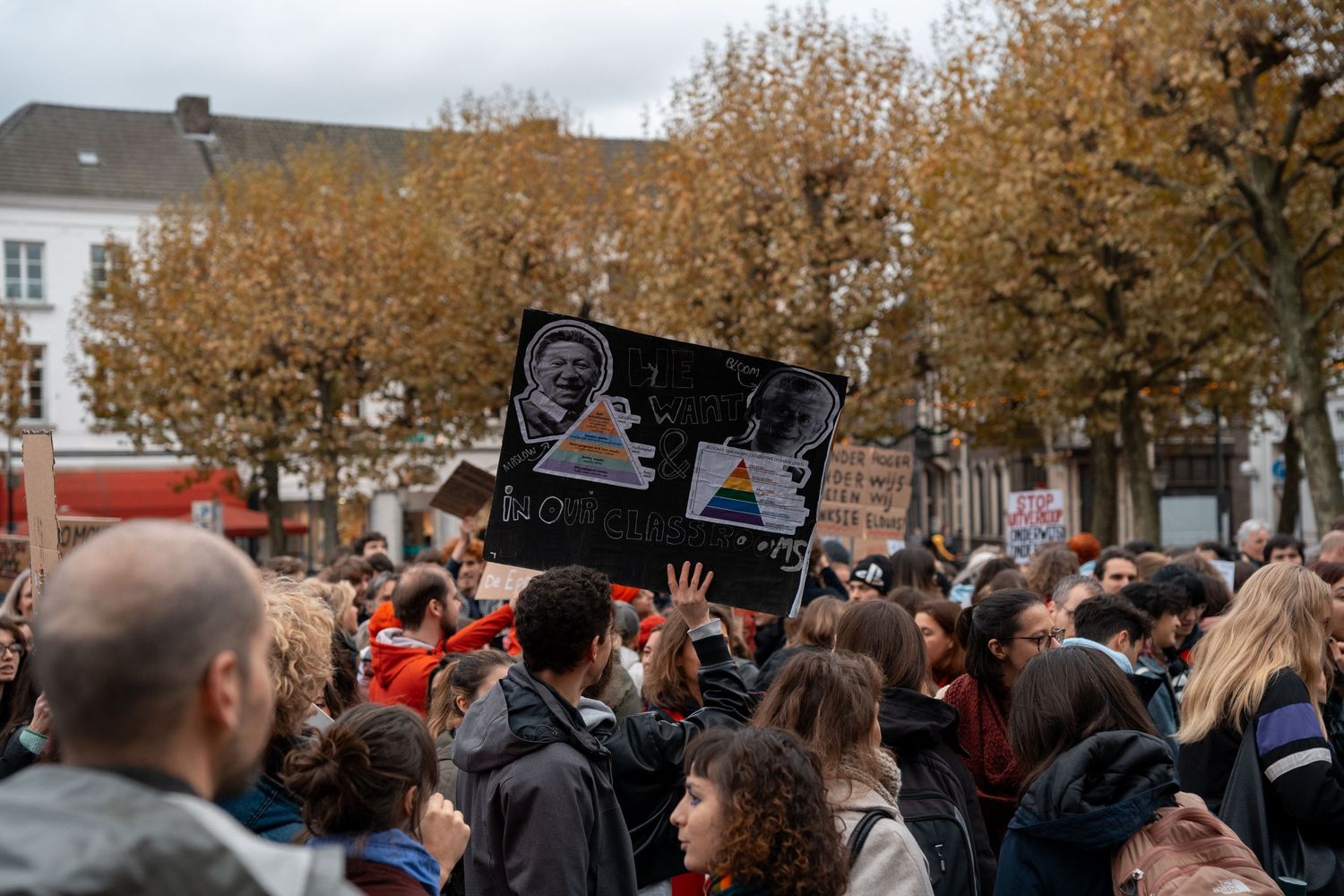 Crowd at student protest rally holding dark Pink Floyd-themed sign outdoors.