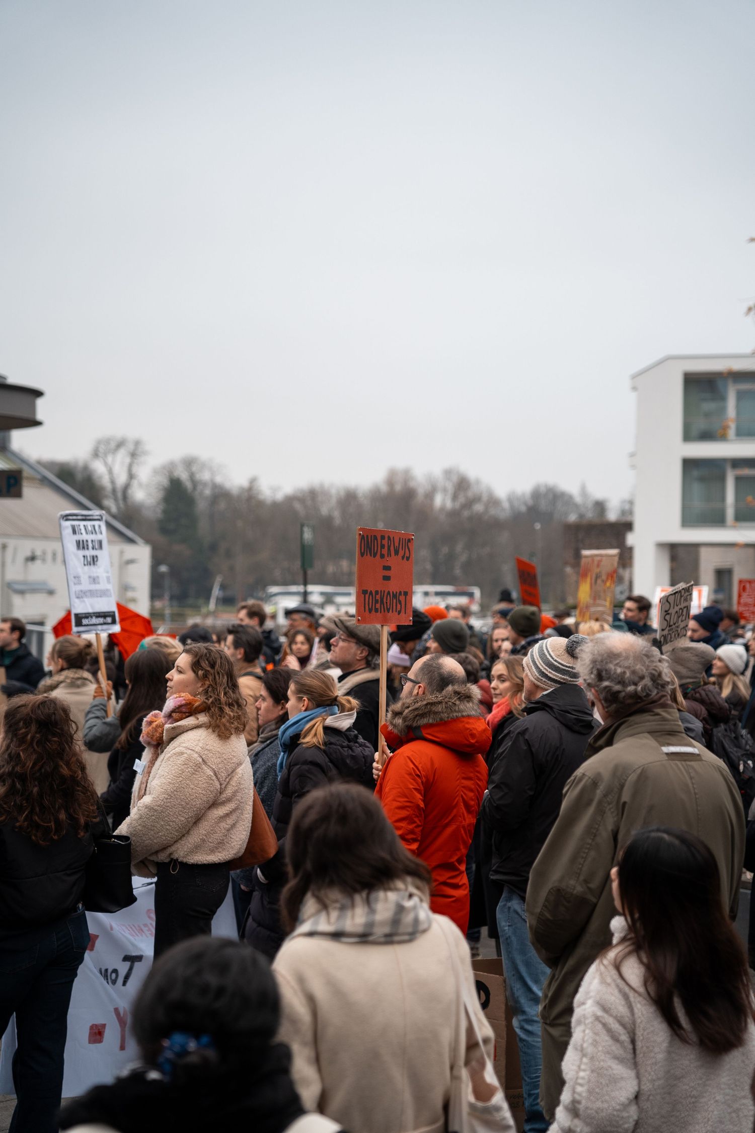 Large crowd of demonstrators holding orange and white protest signs at an outdoor rally.