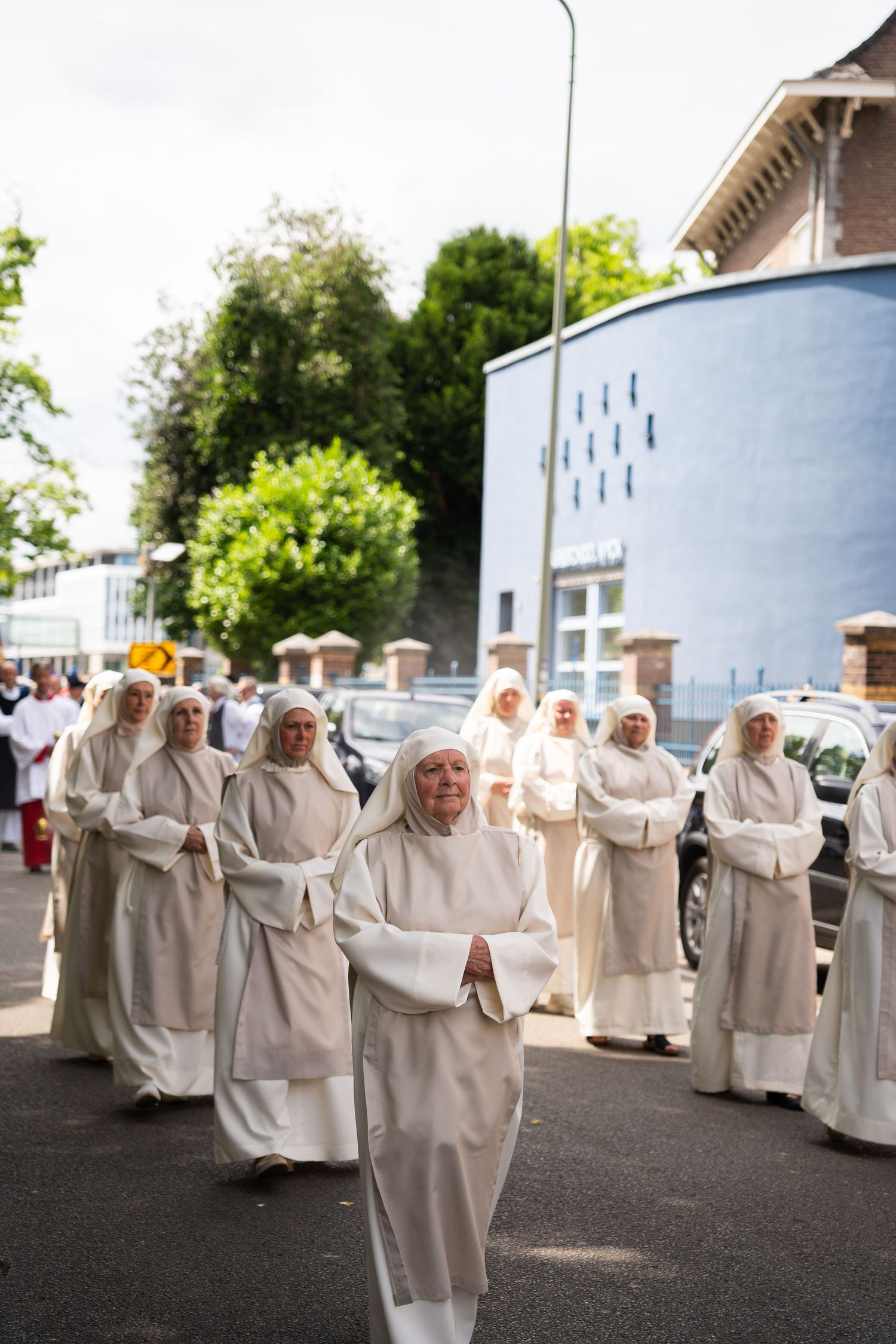 Procession of nuns in white habits walking solemnly along a street during a religious outdoor ceremony.