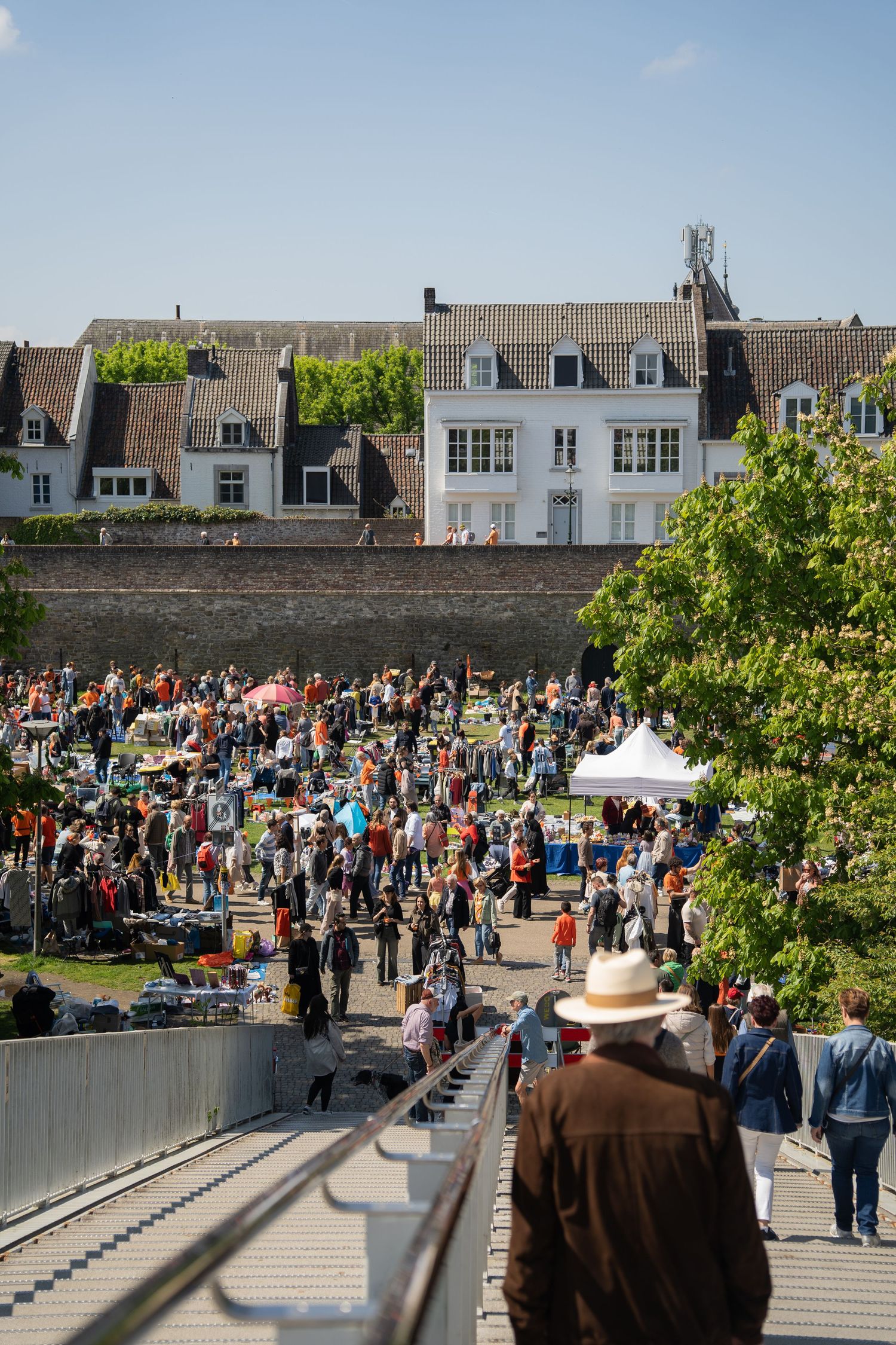 Aerial view of a large outdoor market crowd near historic white buildings on a sunny Kings Day.