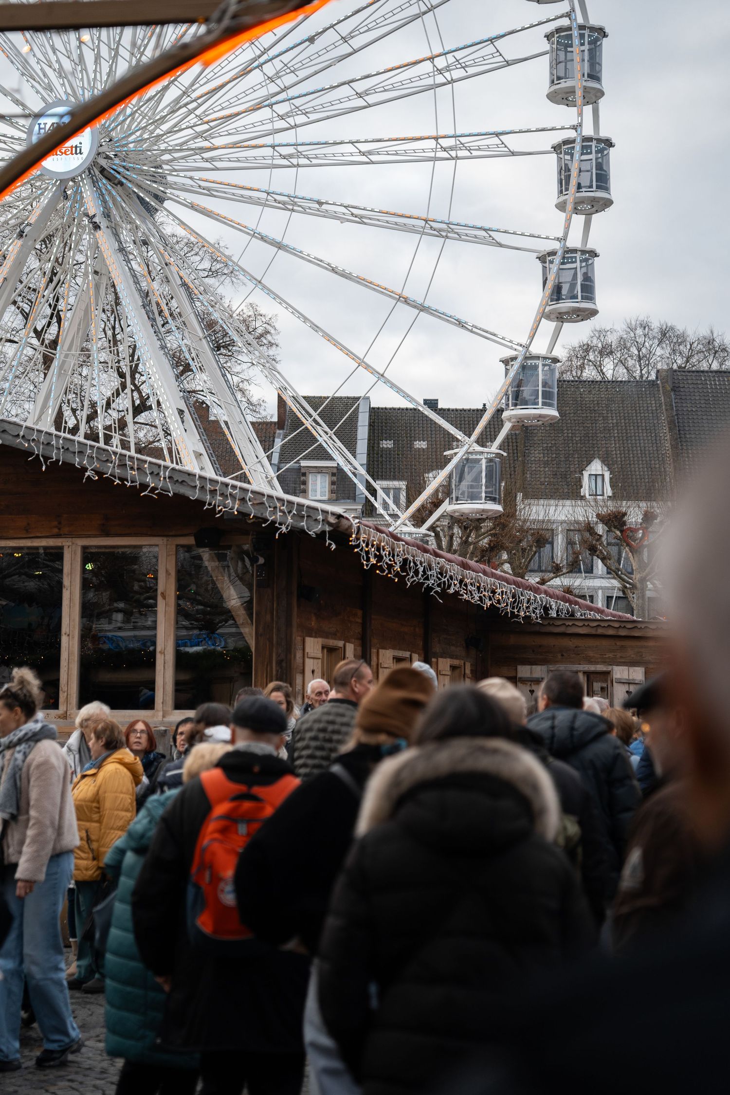 Crowds of visitors at a Christmas market with a large white Ferris wheel visible in the background.