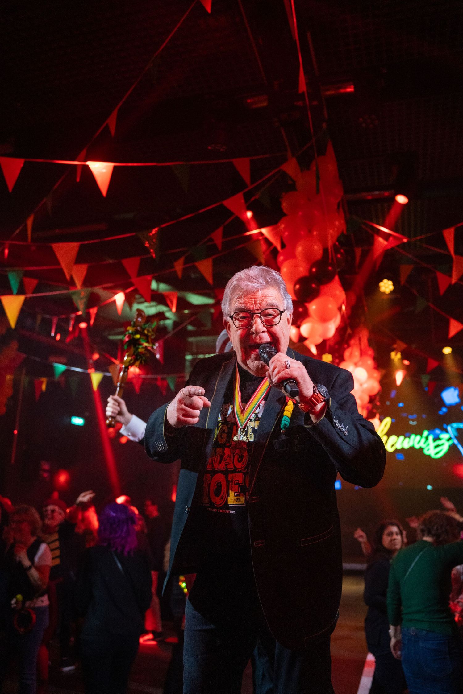 Elderly man performing on stage with microphone at a colorful carnival party with bunting.