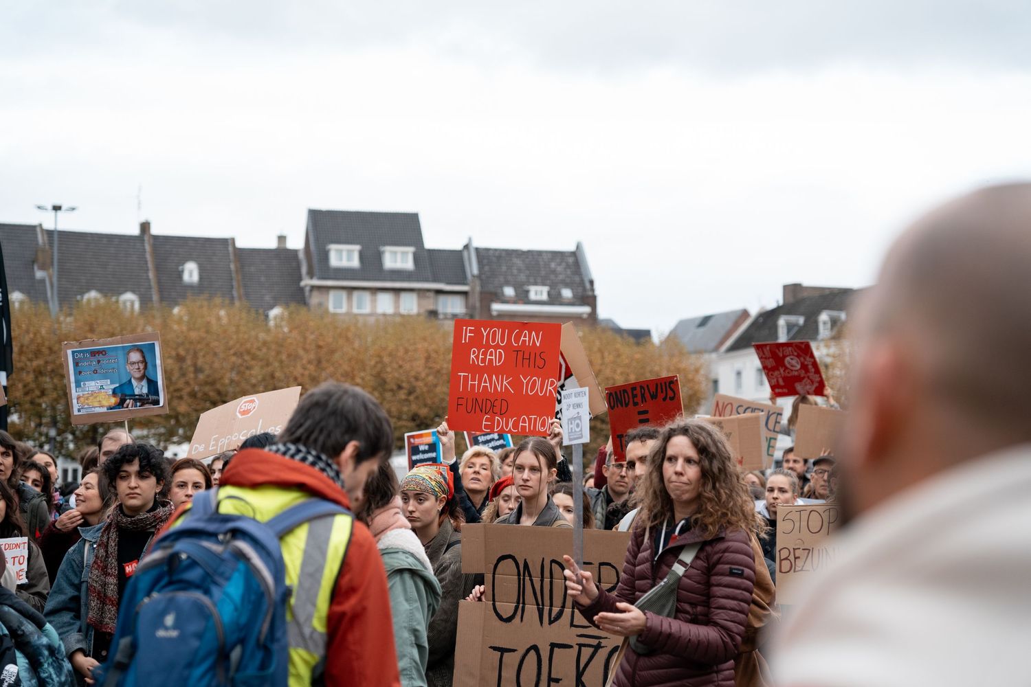 Students march in protest carrying colorful signs at an outdoor demonstration in autumn.