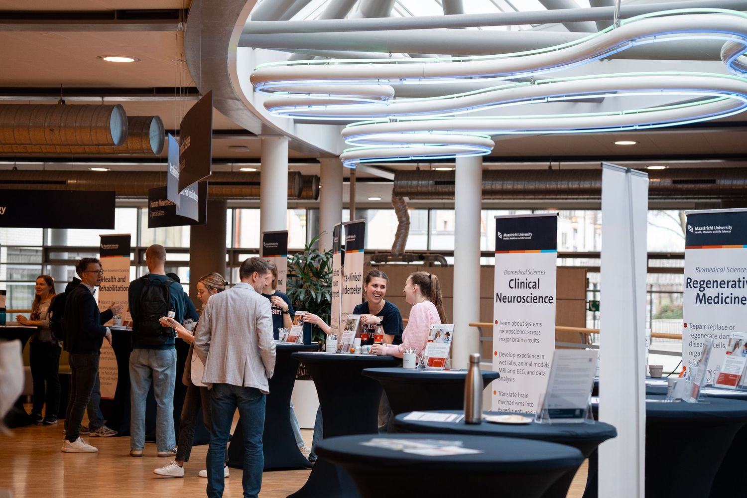 Professionals networking at a university career fair with clinical neuroscience and medicine exhibition stands.