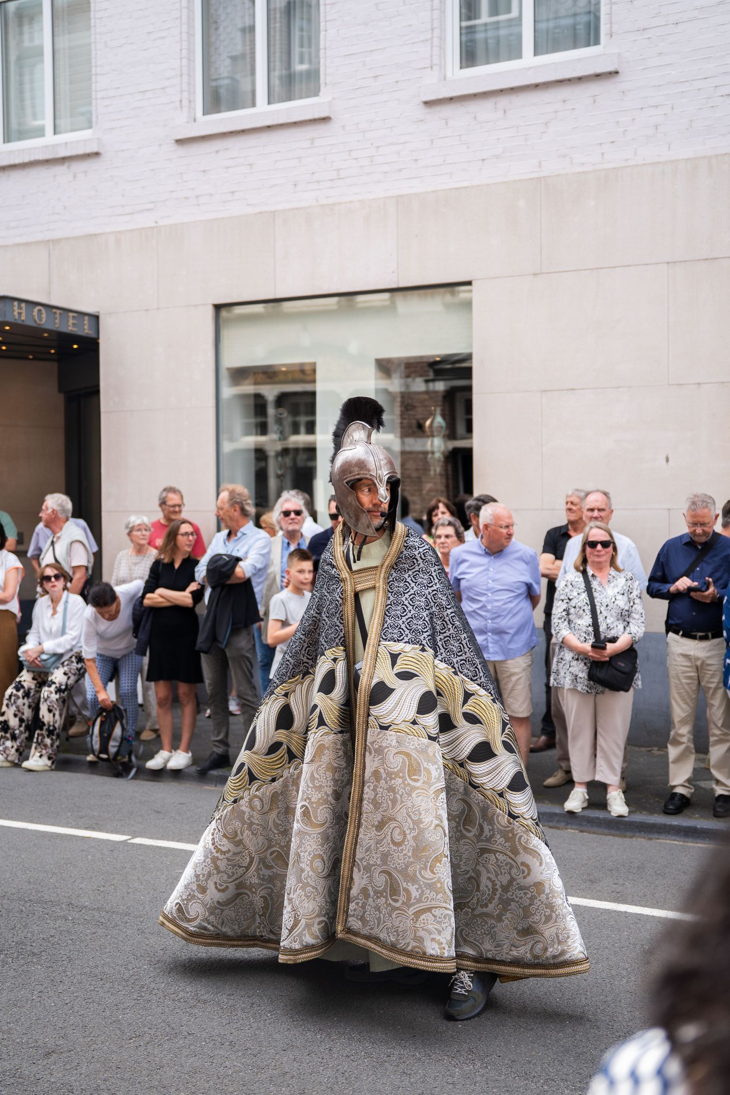 Performer in elaborate medieval costume with helmet and ornate cape marches in a street parade.