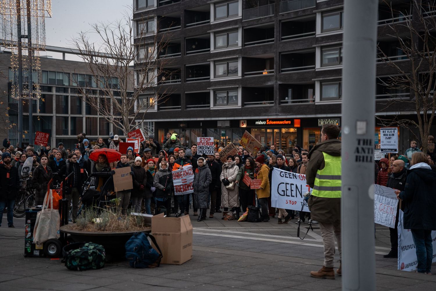 Crowd of protesters holding signs demonstrate in a city square on a winter day.