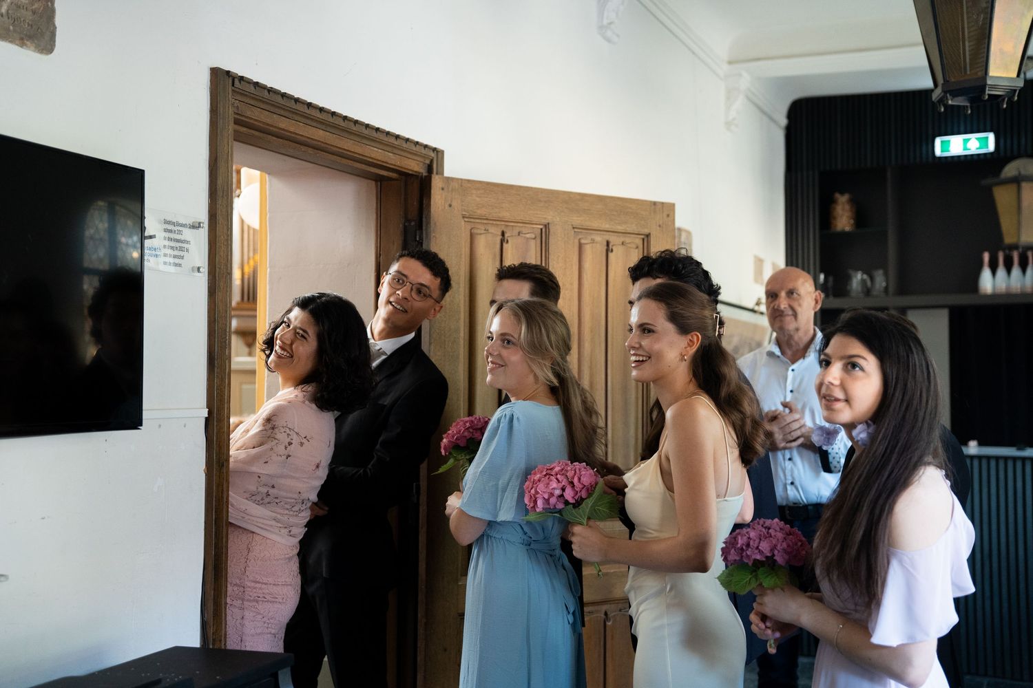 Wedding party group gathered together indoors holding pink flowers at a celebration.