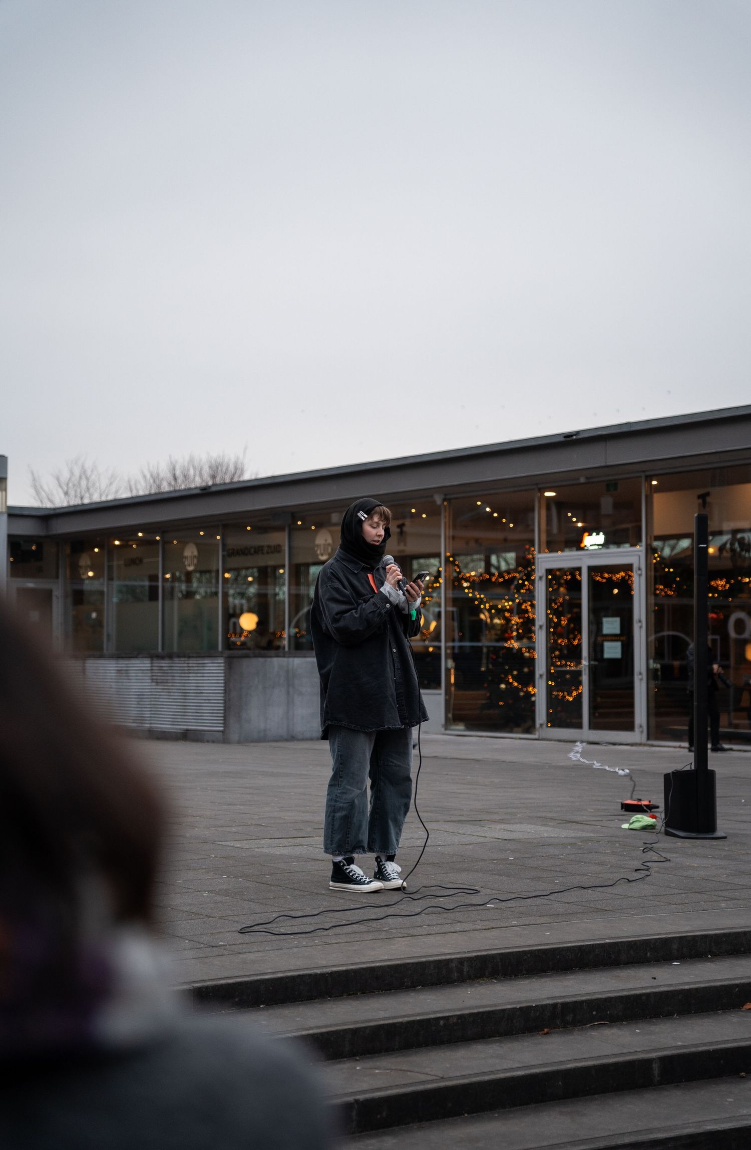 A young woman speaks into a microphone at an outdoor protest rally on a cloudy day.