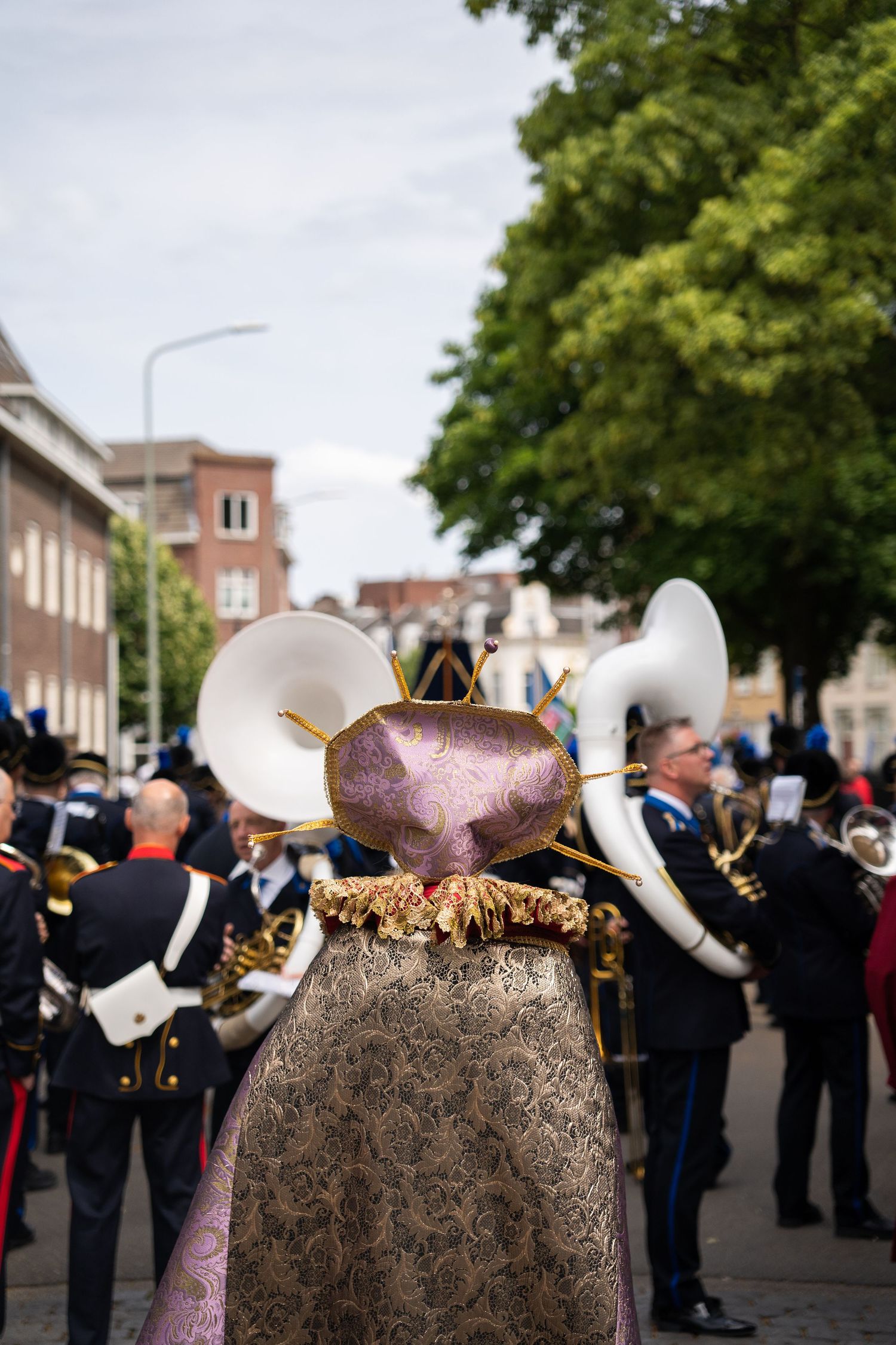 Rear view of a drum major in ornate costume leading a brass band during an outdoor street parade.