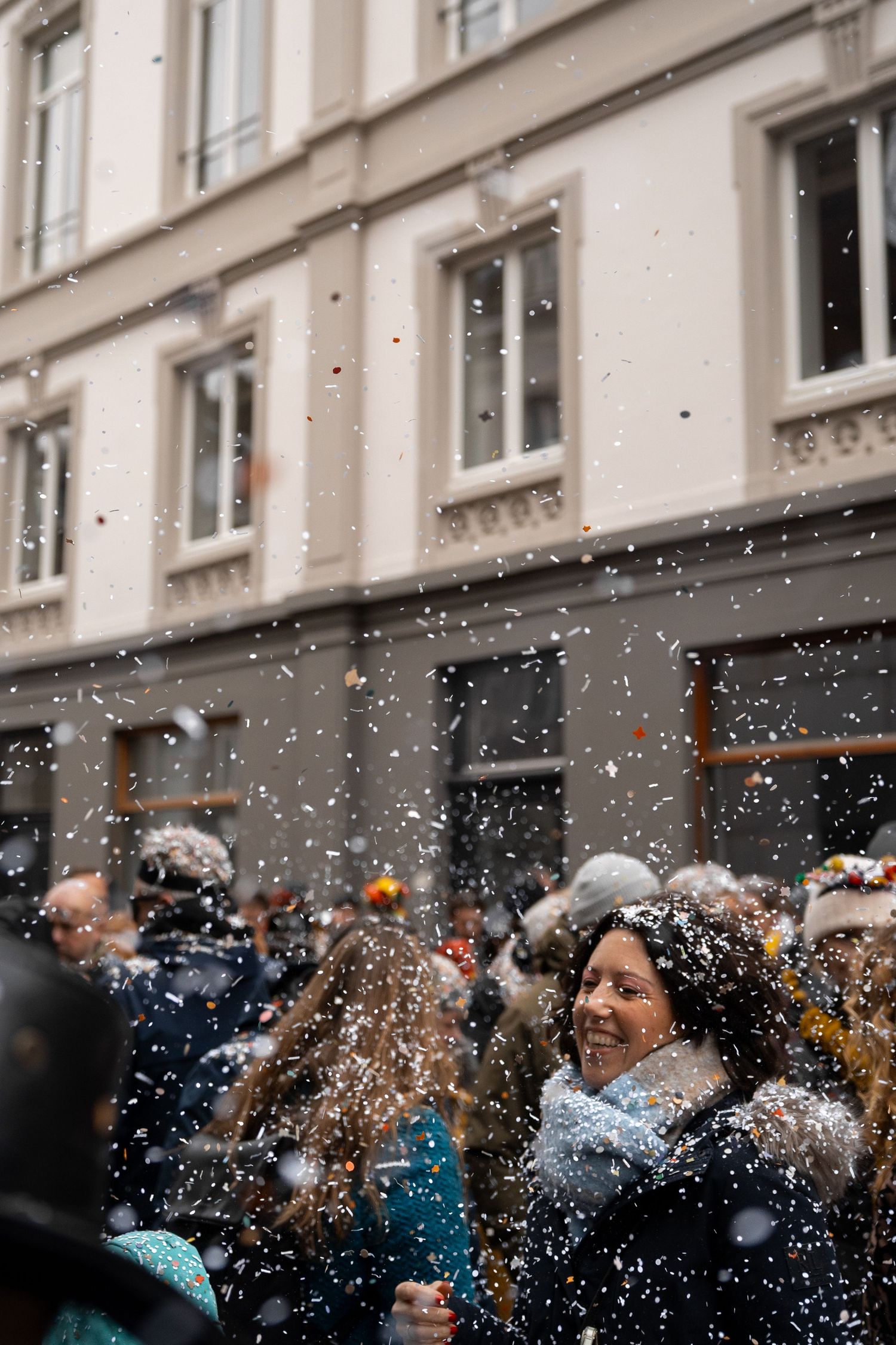 Smiling woman enjoying a shower of confetti during a lively winter street carnival parade celebration.