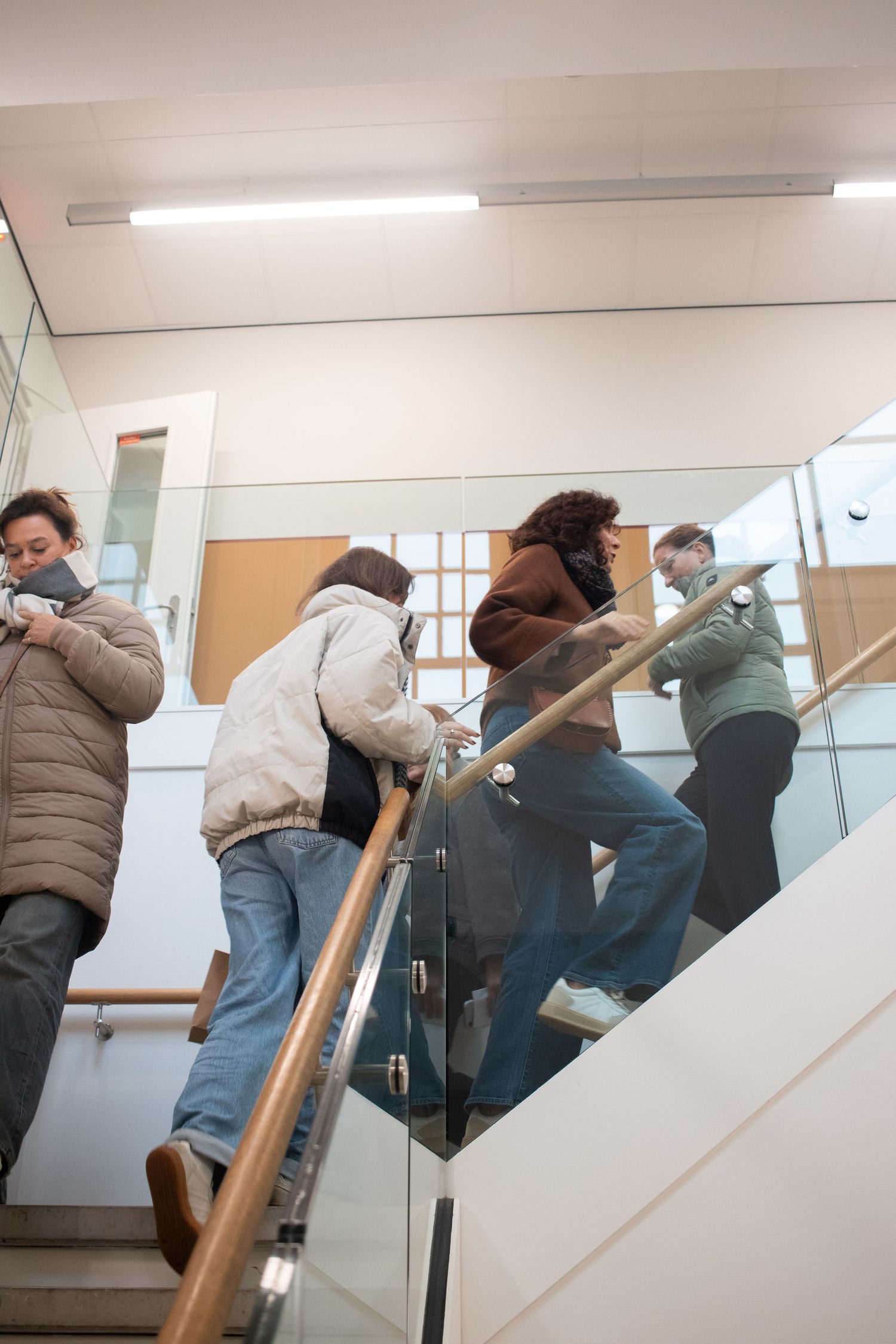 University students walk up a modern staircase with glass railings inside an academic building.
