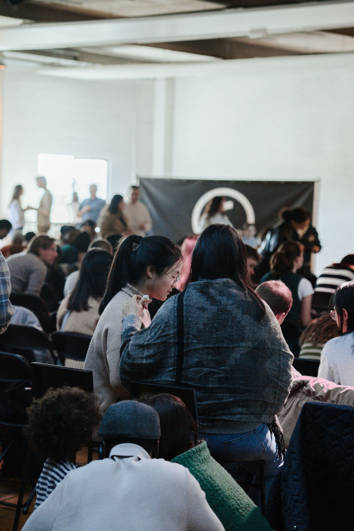Diverse congregation seated in chairs during a church service with a dark banner displayed at the front.