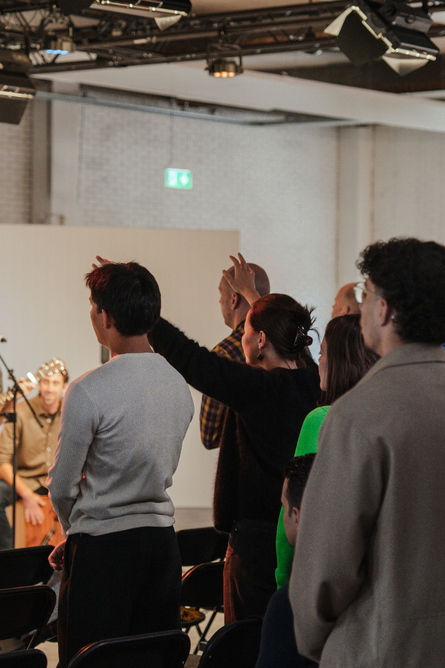 Congregation members raise hands in praise during live worship band performance at church service.