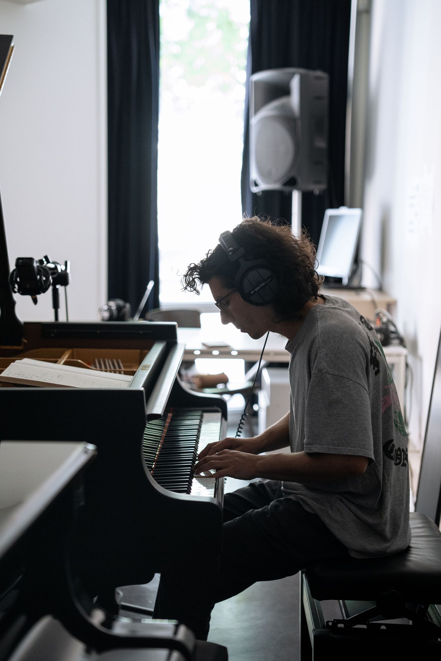 Musician with headphones plays a grand piano in a professional recording studio setting.