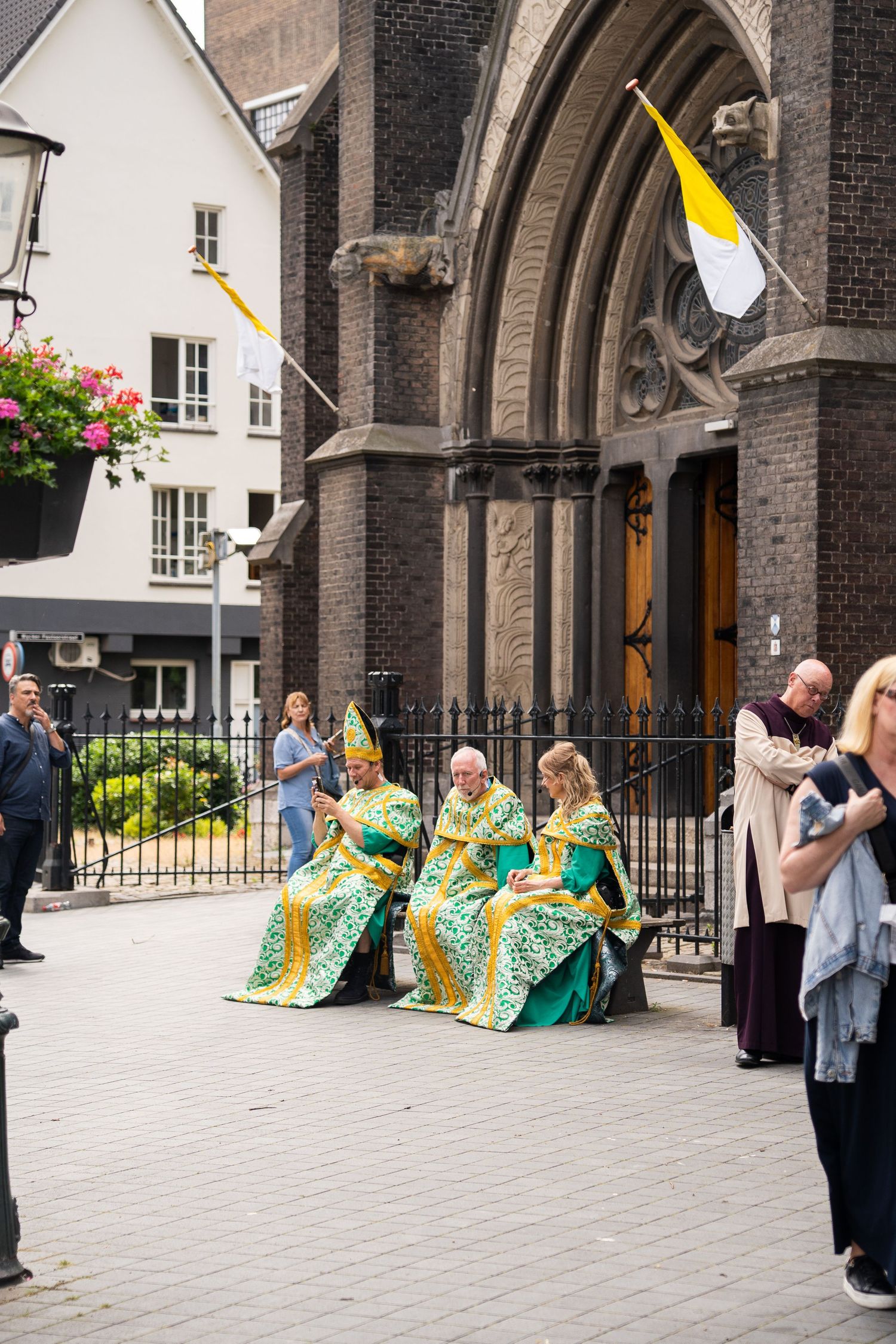 Clergy in green and gold vestments rest outside ornate brick church entrance.