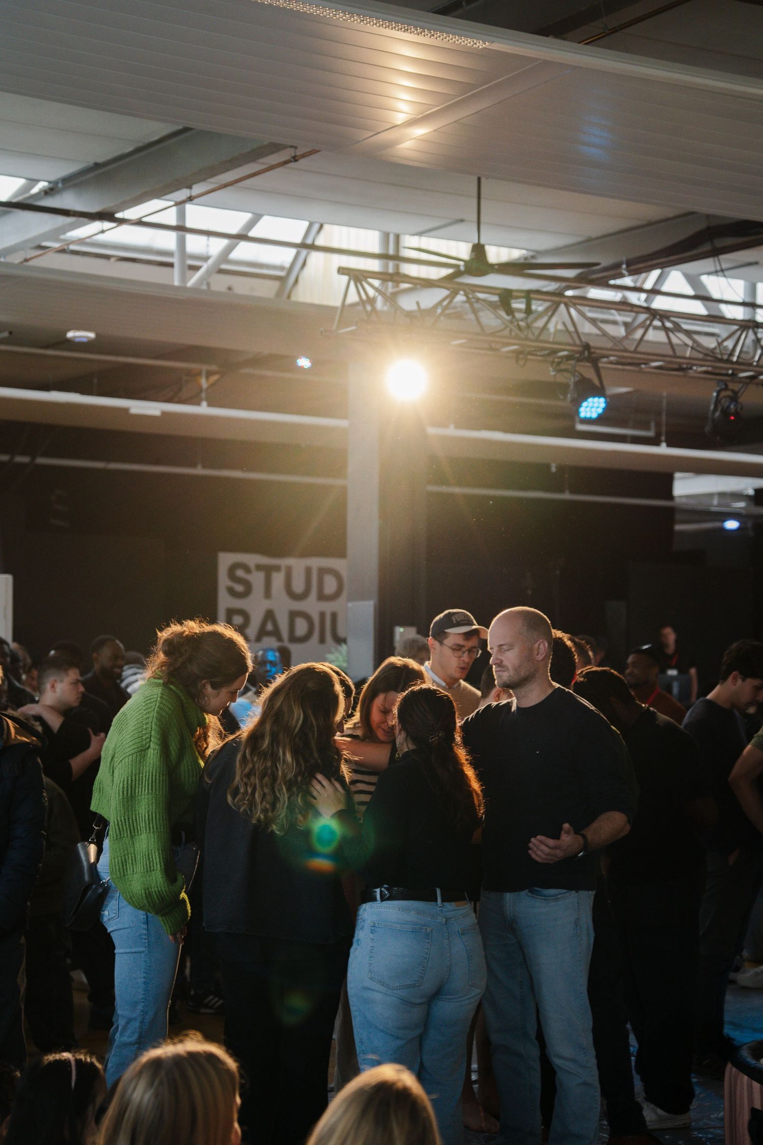 Crowd of people gathered under warm stage lighting at an indoor event with a sign reading Studio Radil.