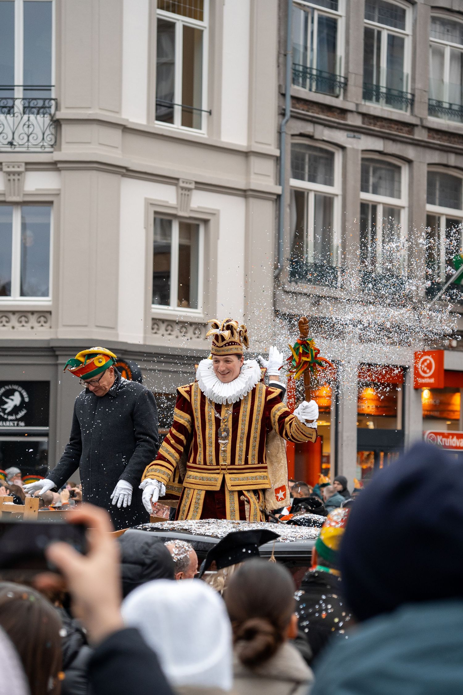 Elaborately costumed carnival king throwing confetti into the crowd from a float during a winter street parade.