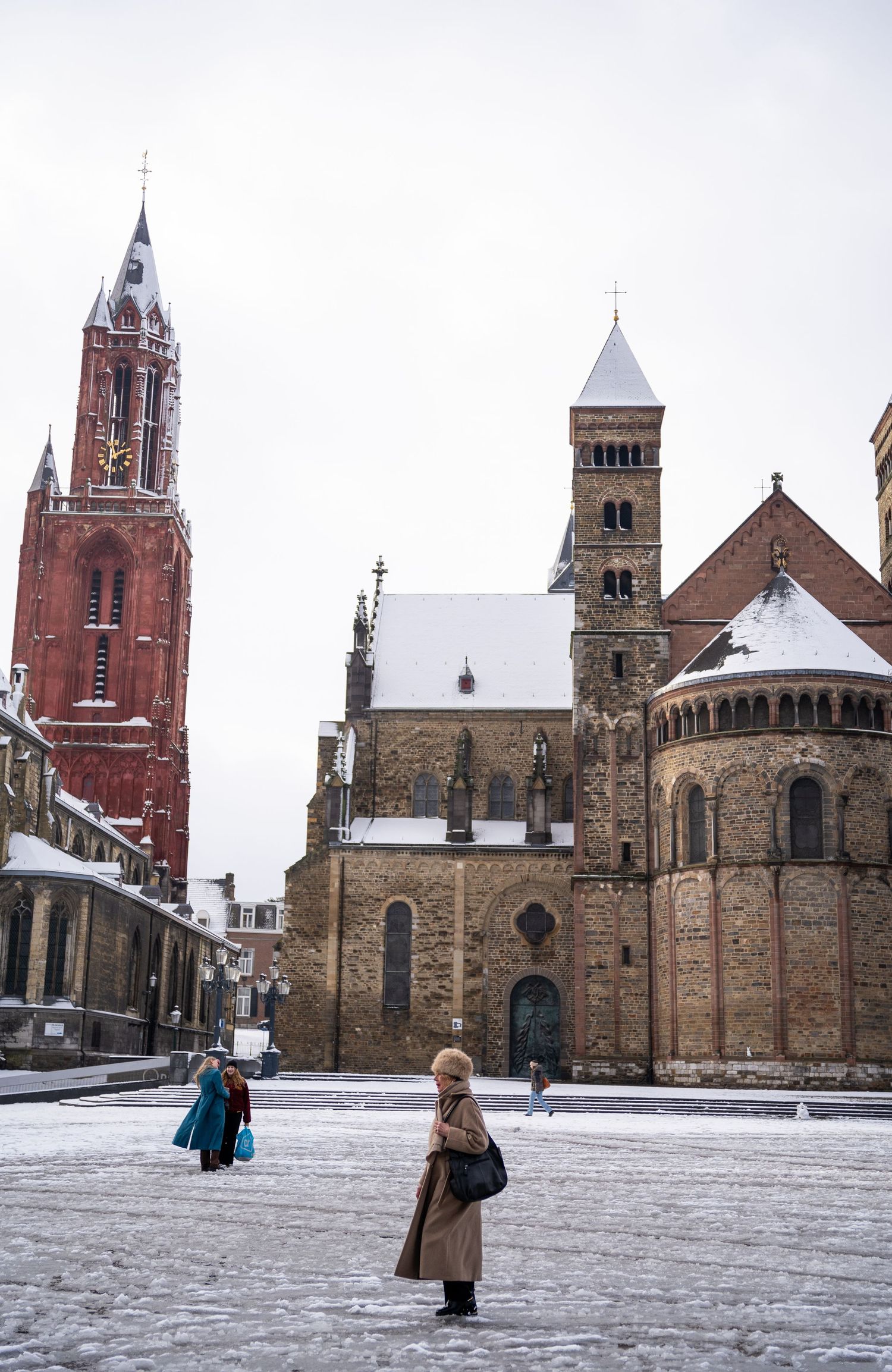 A woman stands in a snow-covered Vrijthof square with the Sint-Janskerk and Basilica of Saint Servatius in Maastricht.