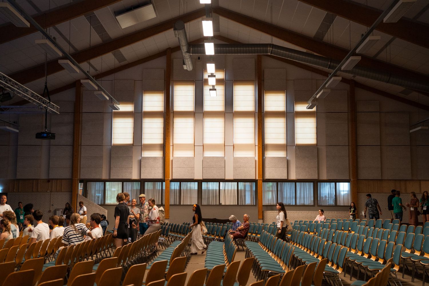 Spacious wooden church hall with rows of chairs and large windows during a daytime gathering.