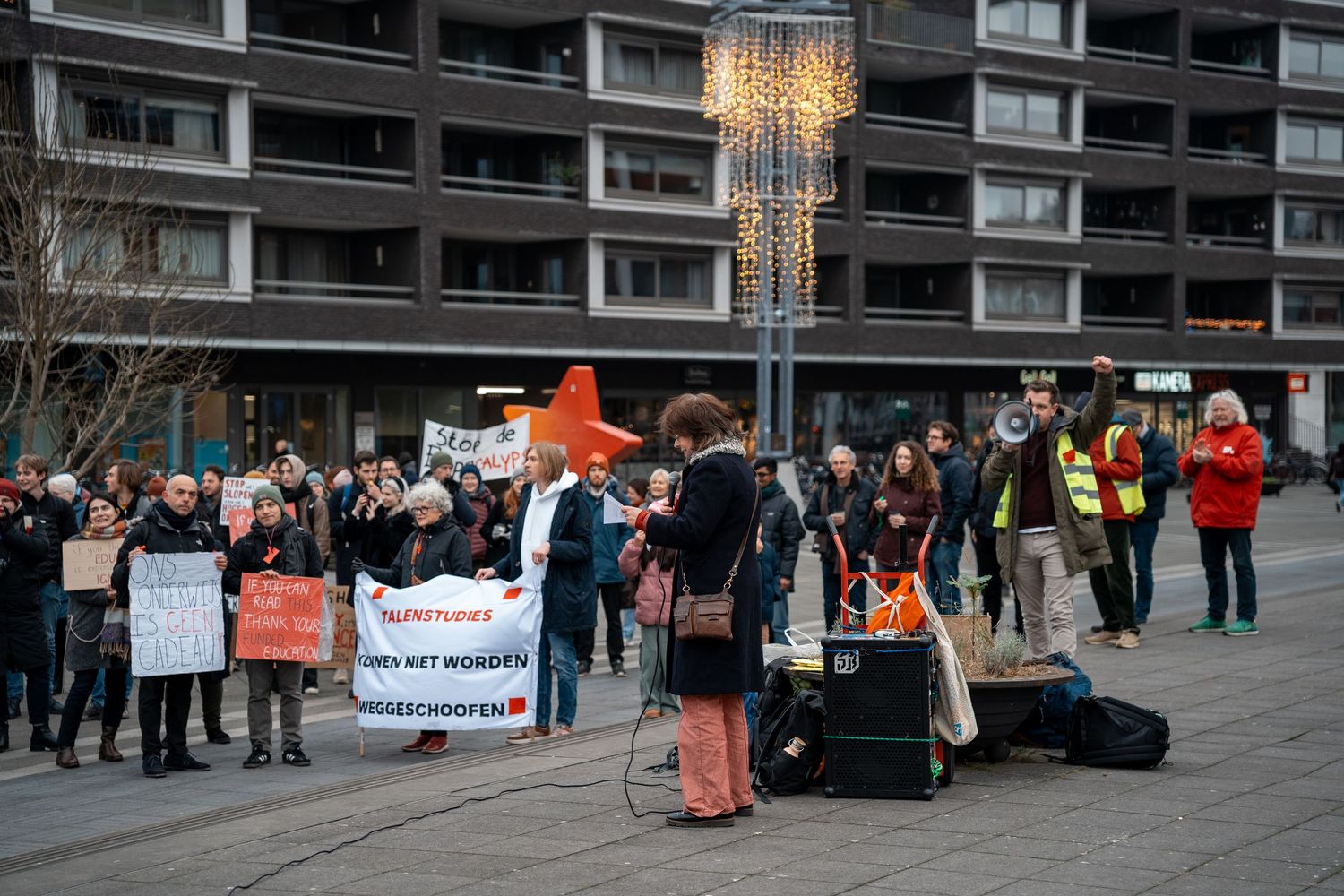 Protesters gather in a town square holding banners and signs during a demonstration against academic budget cuts.