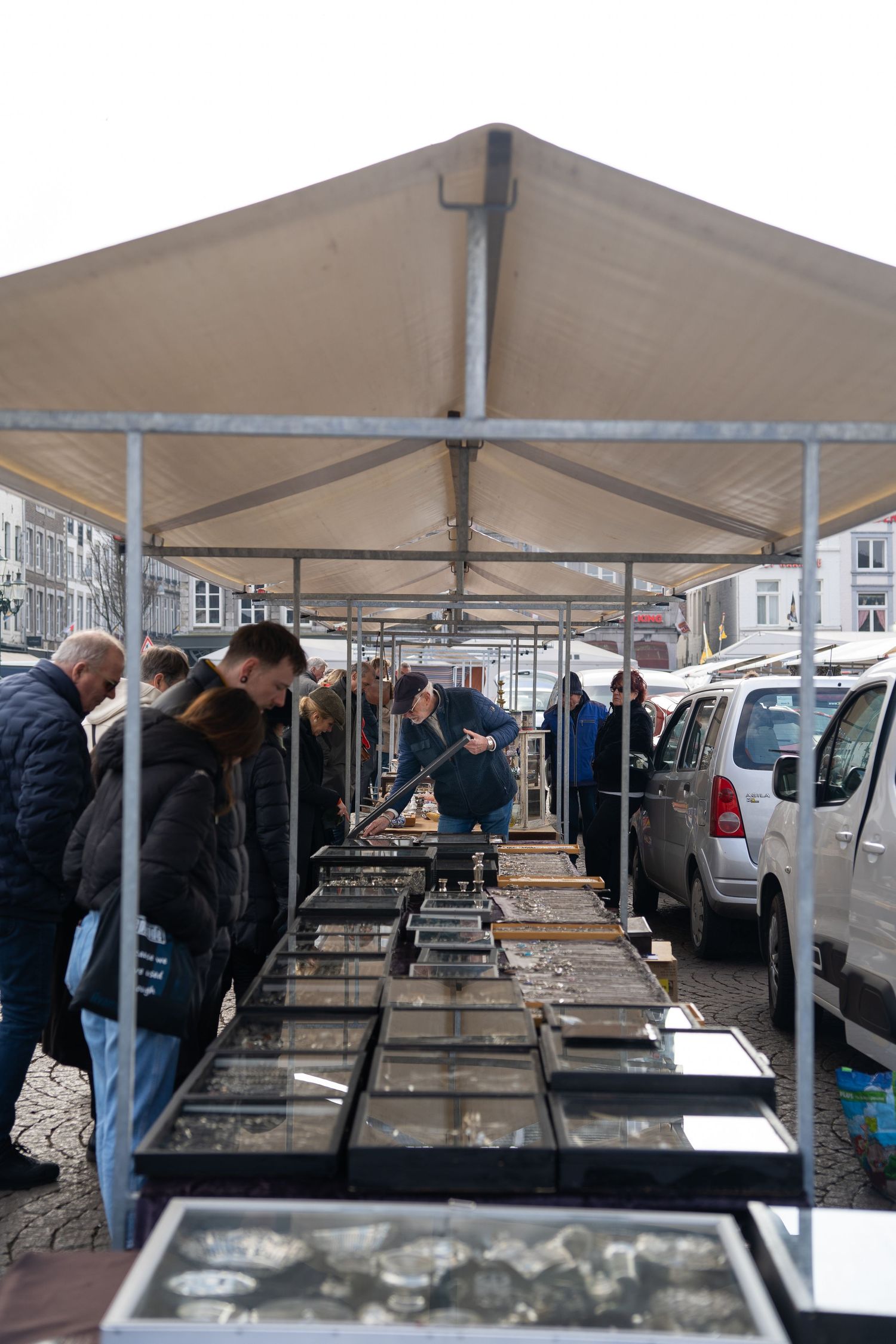 People browsing collectible coins and antiques at an outdoor market stall under a white canopy tent.