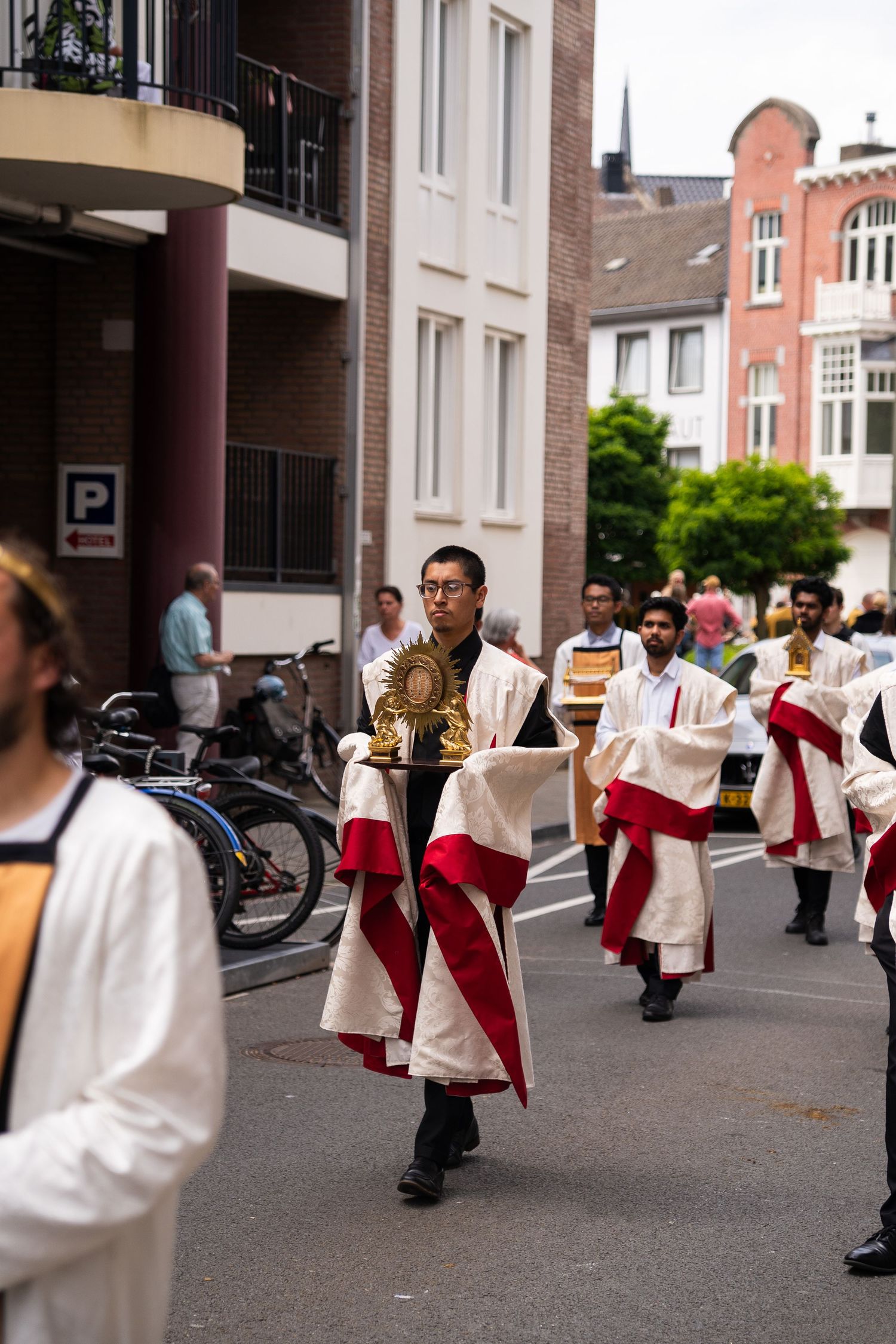 Catholic procession with robed participants carrying golden monstrance through urban street.