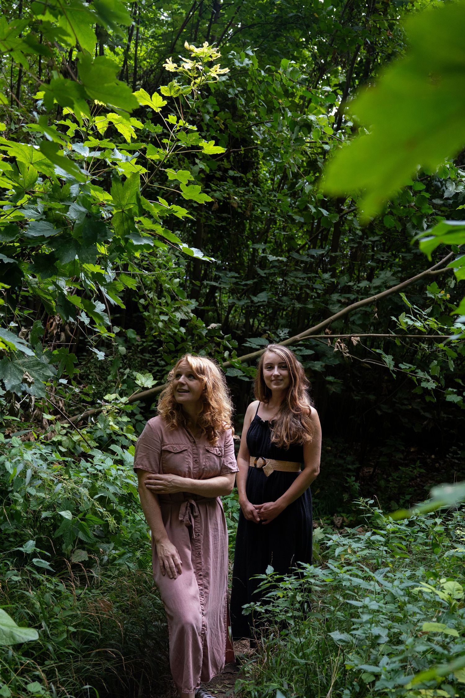 Two women standing on a forest path surrounded by lush green foliage.
