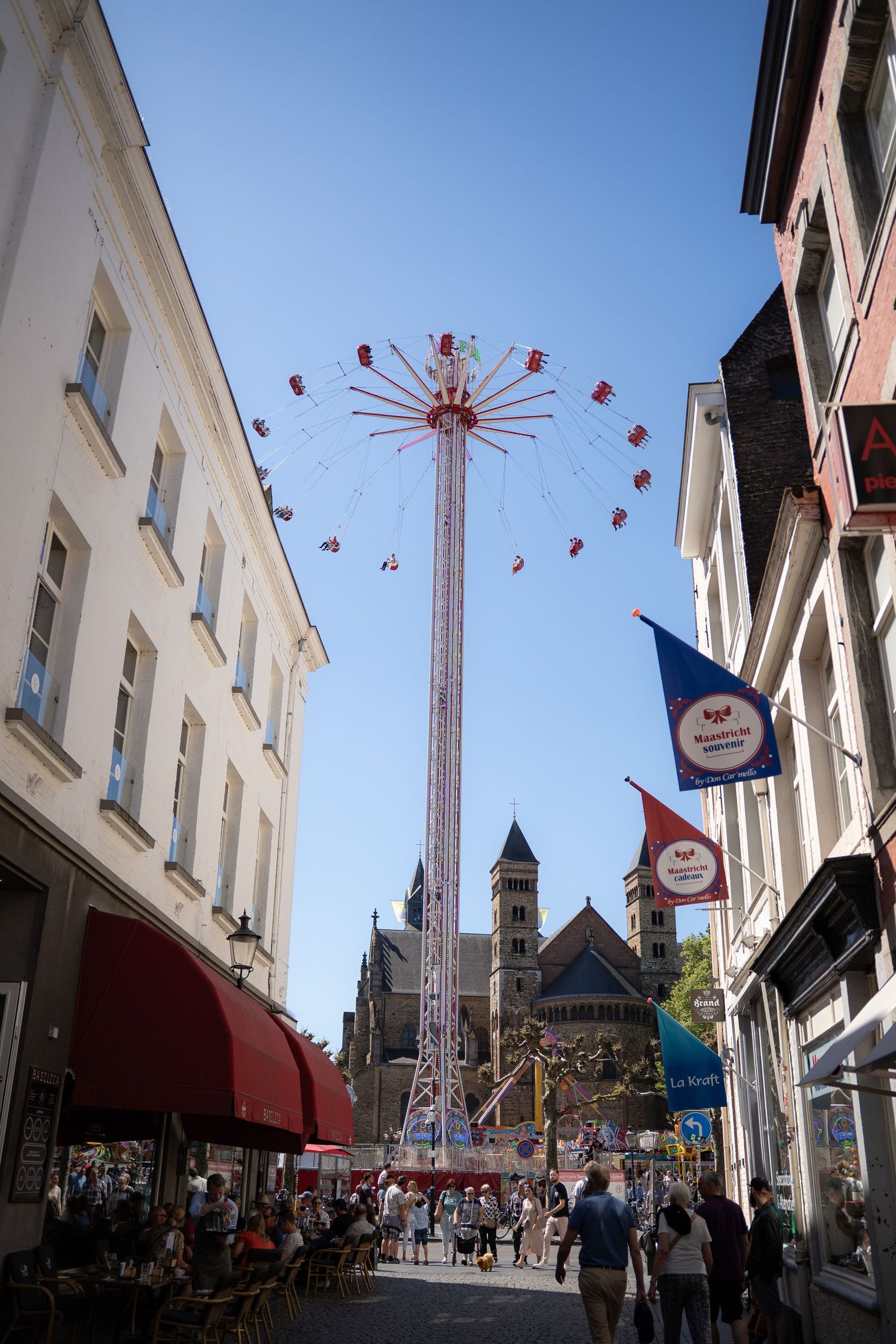 Tall chain swing fairground ride soaring above a busy European street lined with shops and historic buildings.