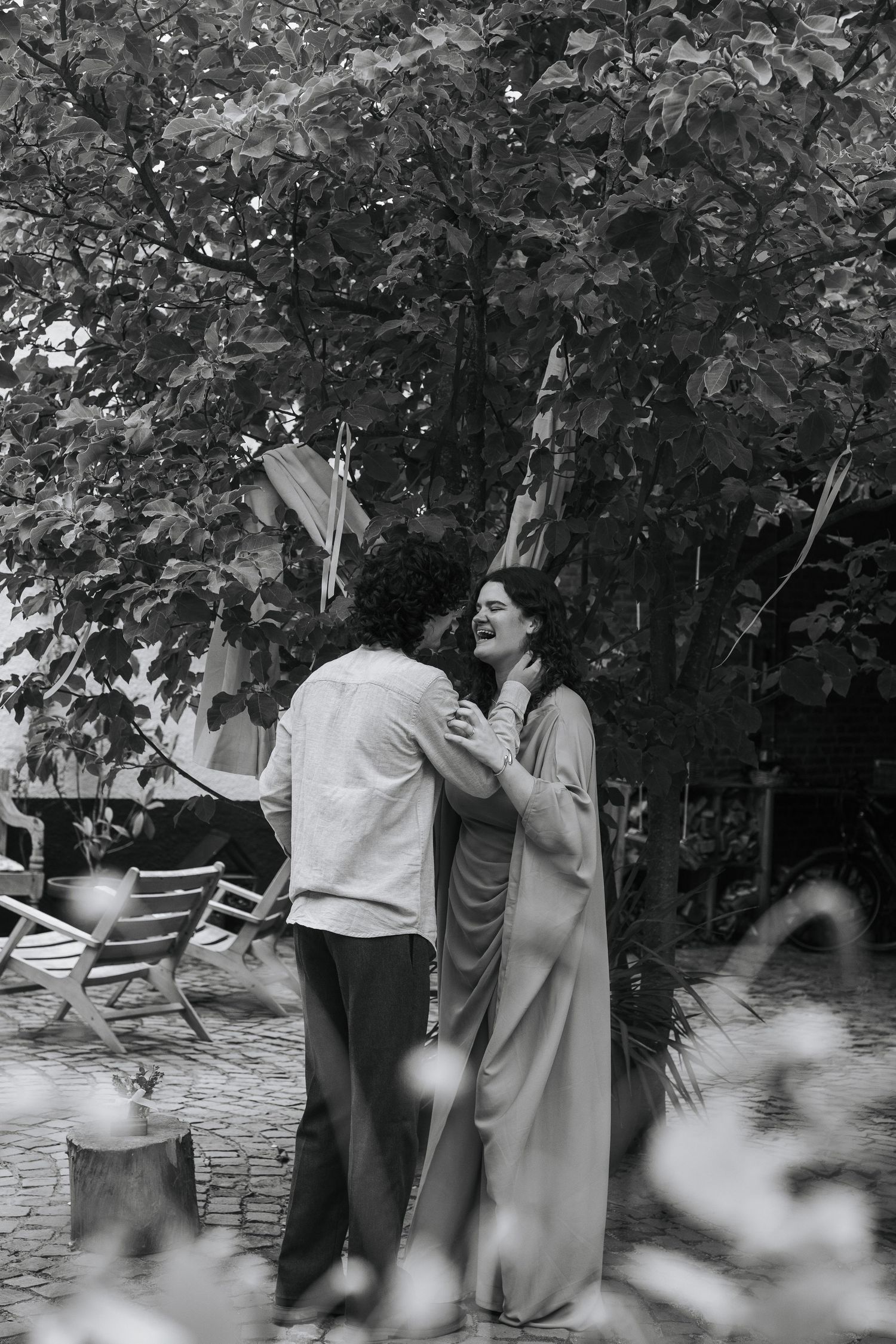 Black and white photo of a couple embracing and laughing in a lush garden setting.